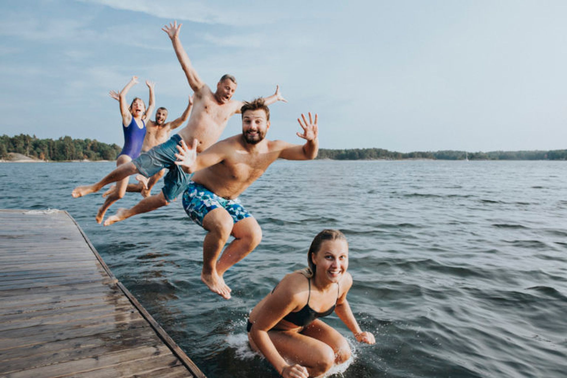 People jumping into a lake from a wooden jetty.