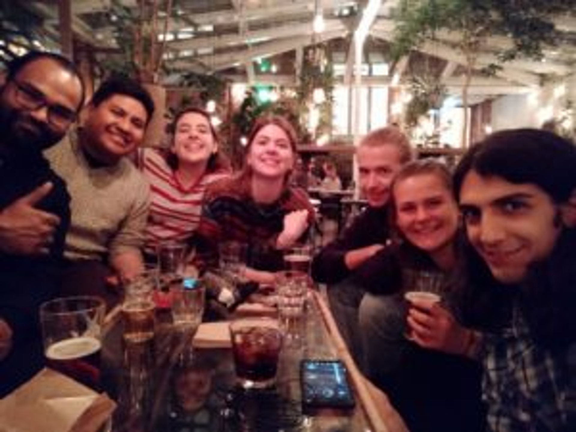 Camilo sits in a bar with a group of friends, drinking beer. 