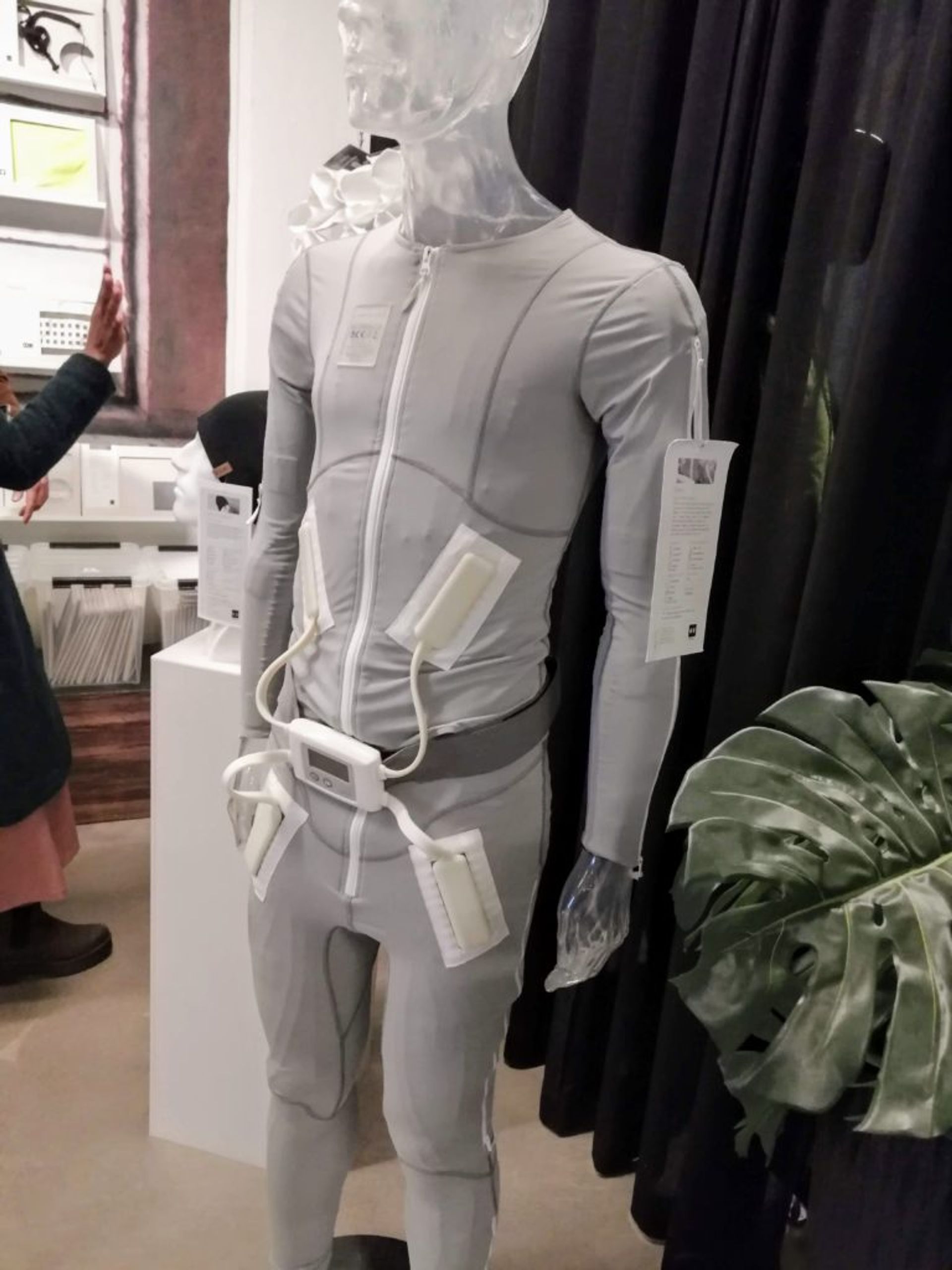 A grey bodysuit on a mannequin with electrical currents attached.