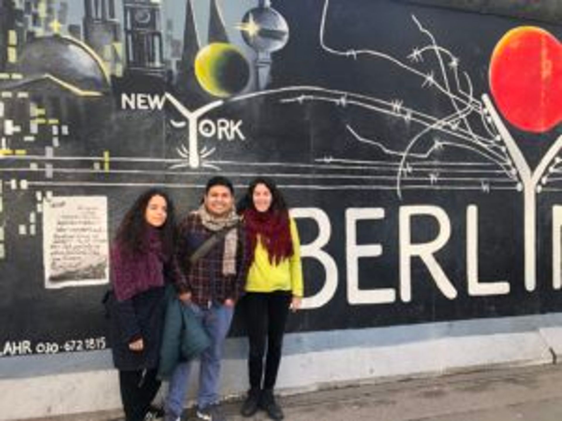 Three people standing in front ot the Berlin wall.