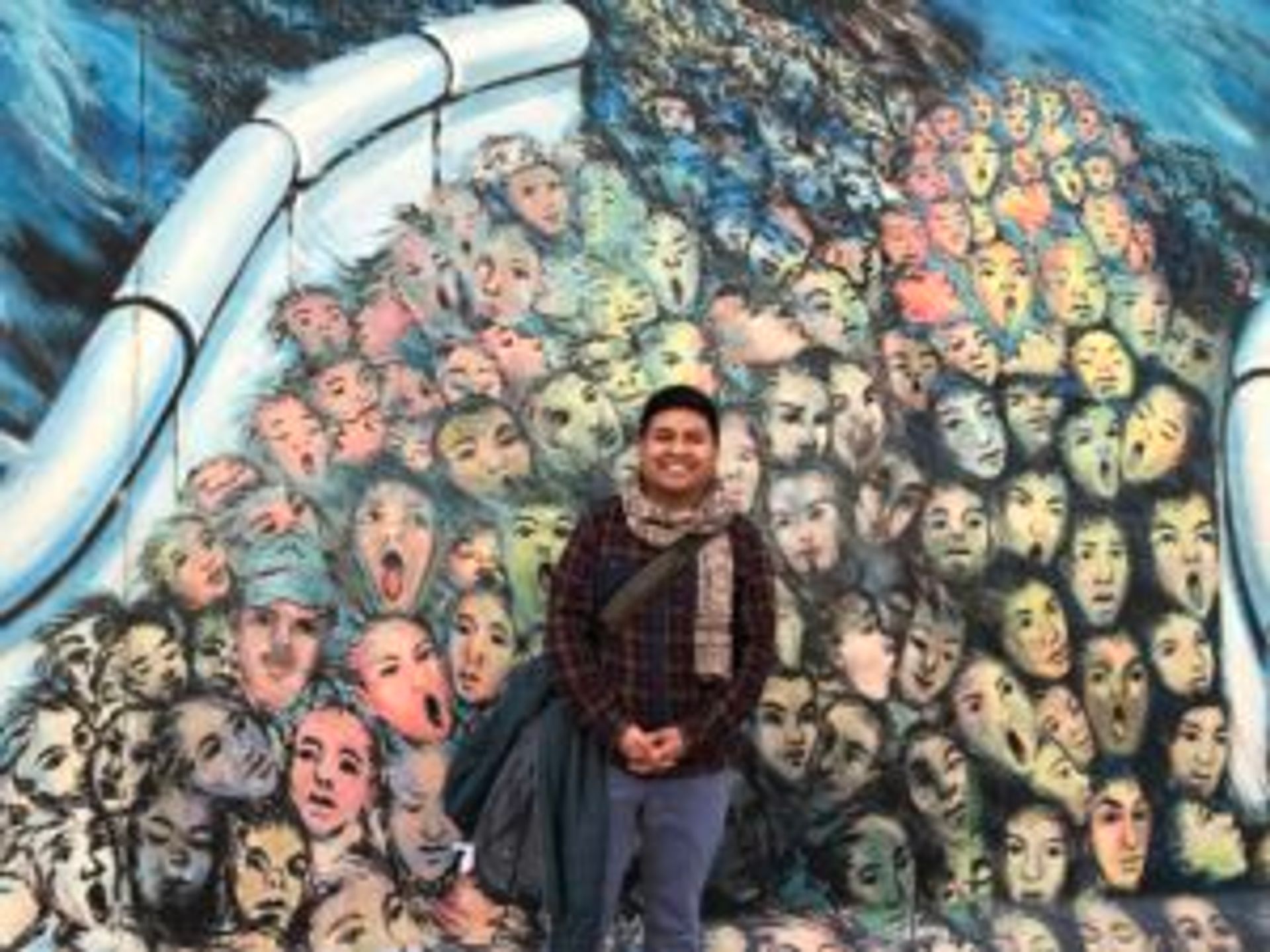 Camilo stands in front of a Berlin wall mural.