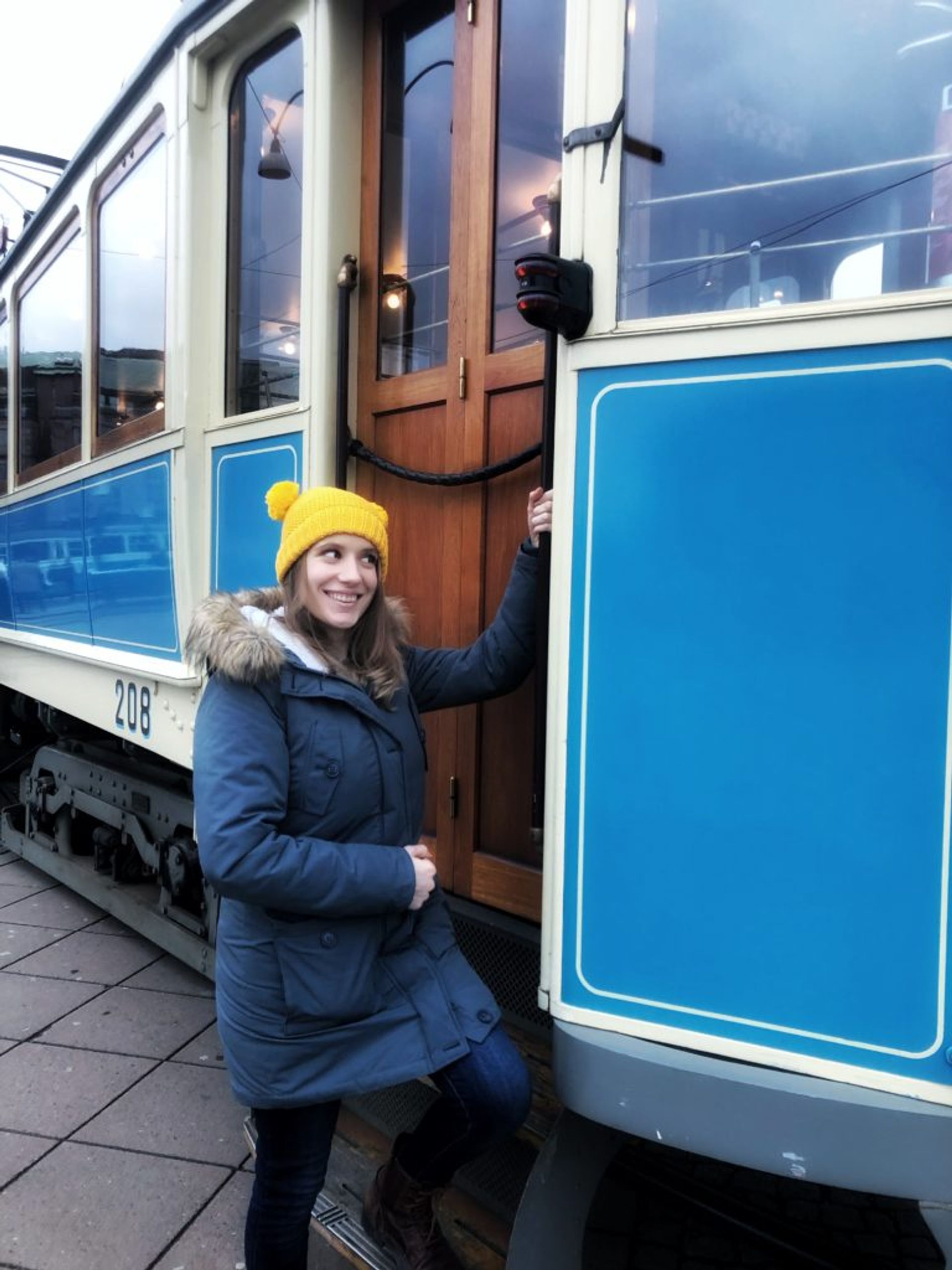 A person standing beside a blue tram.