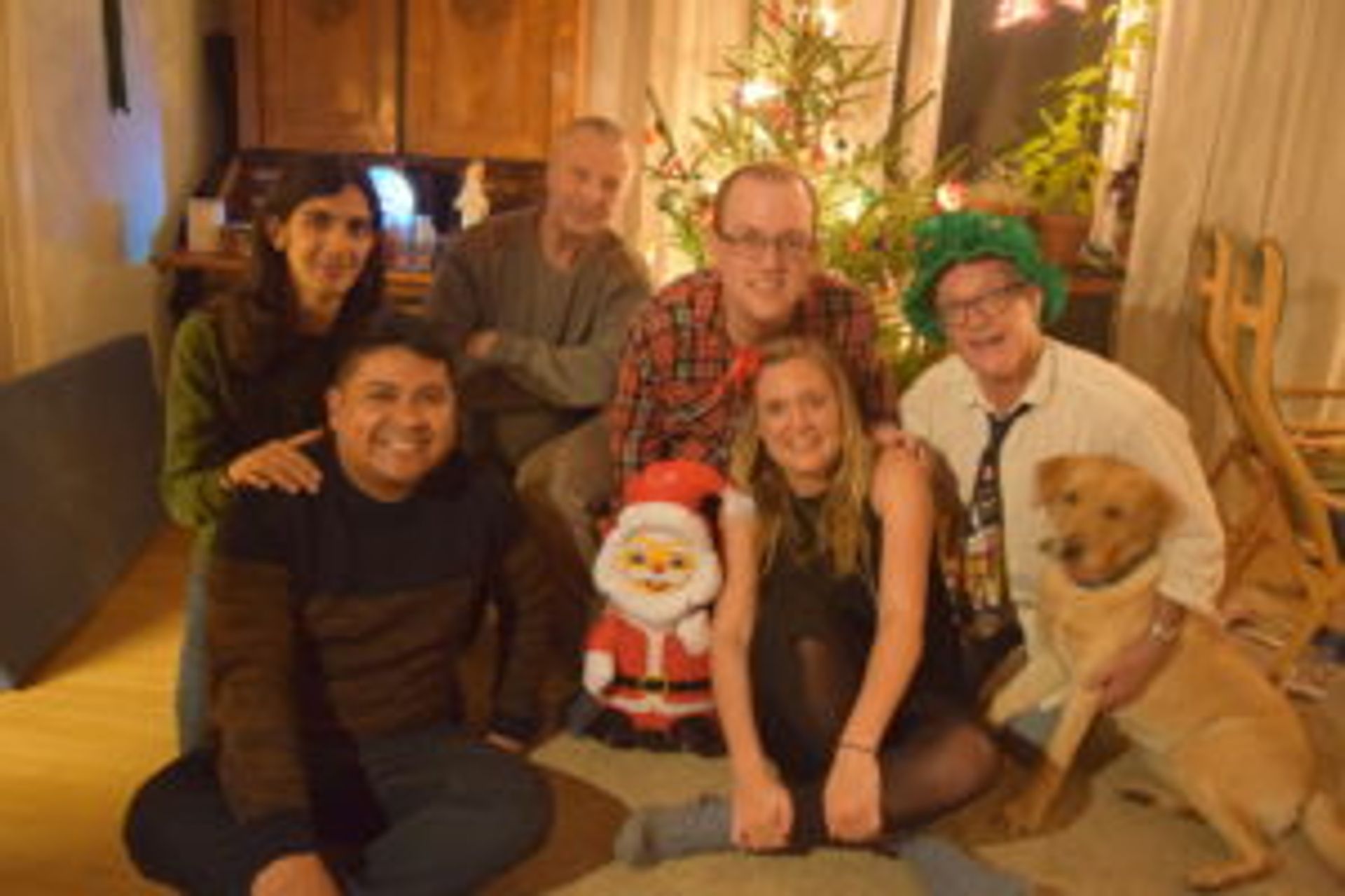 Camilo sits on the floor in front of a Christmas tree together with several people and one dog.