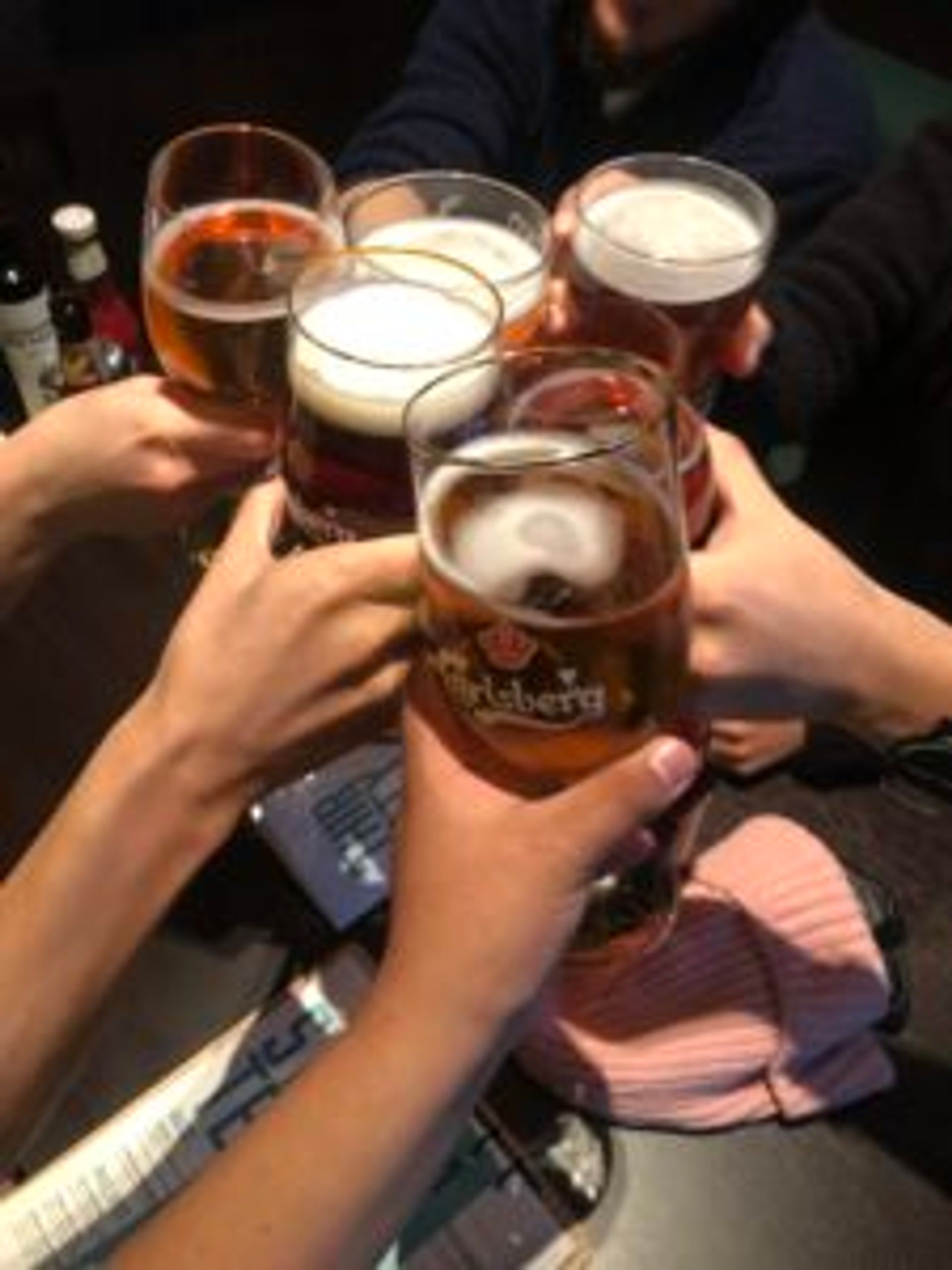 Five people clinking beer glasses in a bar.