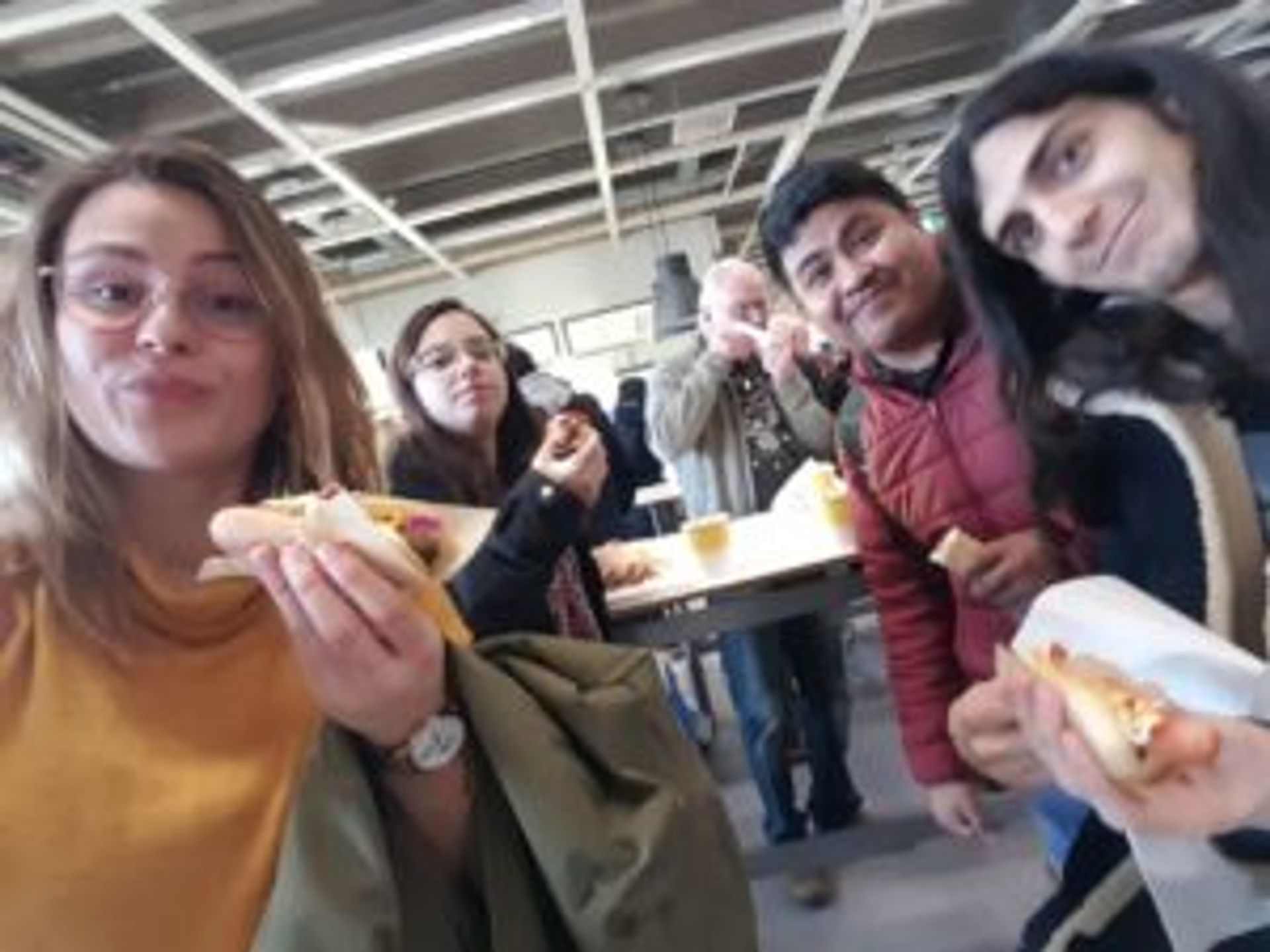 Camilo and several friends eat hotdogs in IKEA.