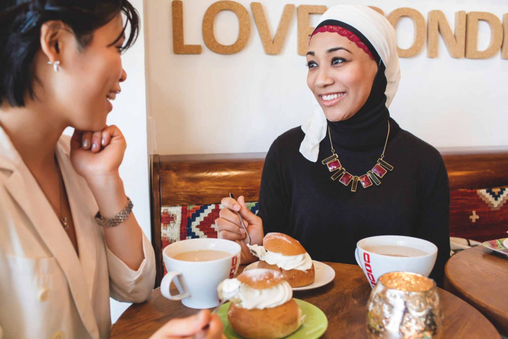 Two women sitting in a cafe drinking coffee and eating semlor - traditional Swedish pastries eaten on Shrove Tuesday.