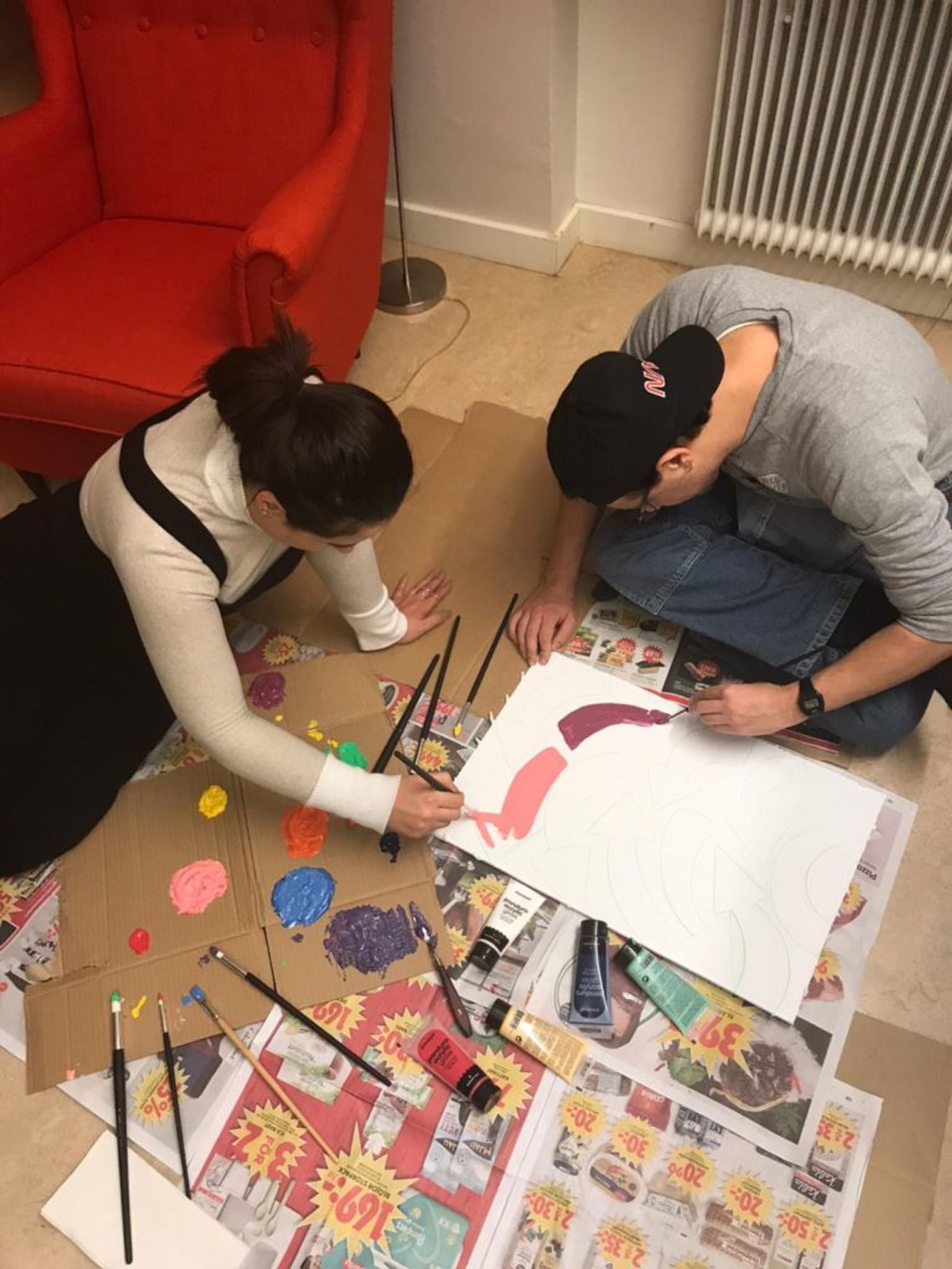 Two students sitting on the floor painting on a white piece of paper.