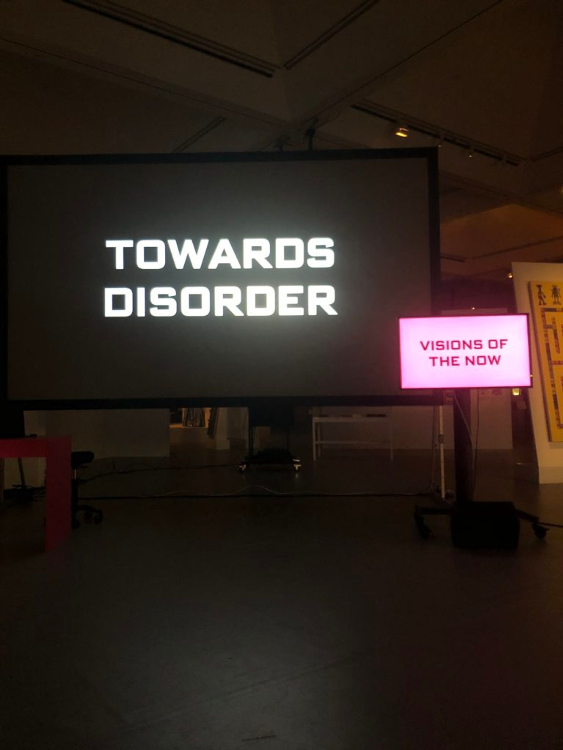 A performance art lecture. There are two screens, captions read 'Towards disorder' and 'Visions of the now'.