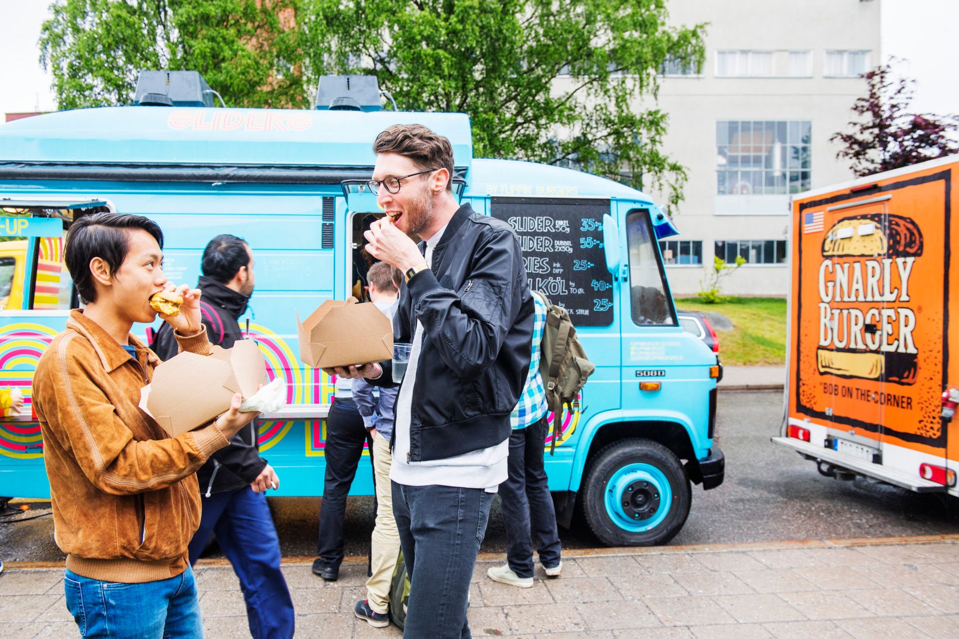 Students standing outside eating food from a light blue food truck.