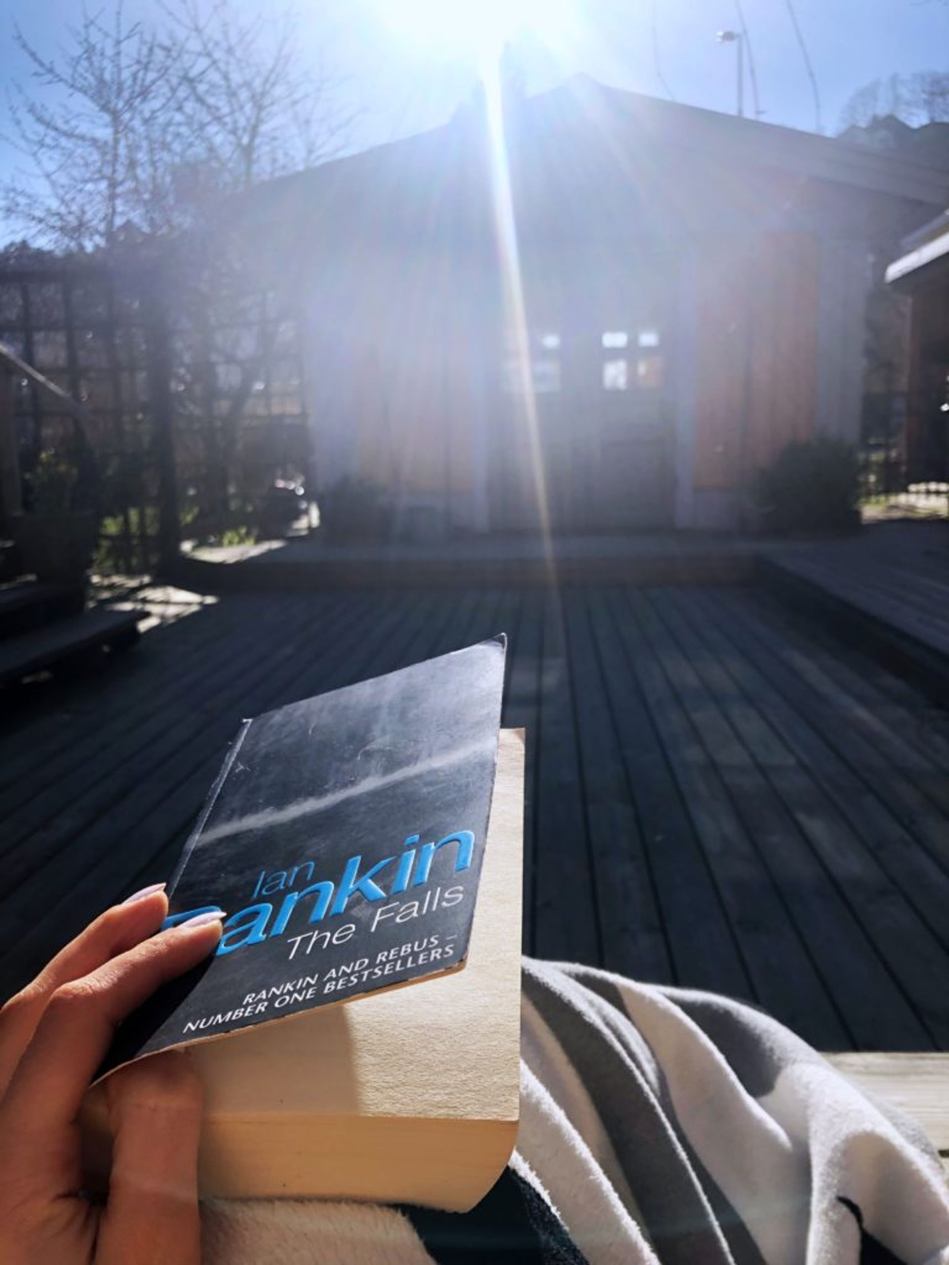 Sara sitting on the patio rading an Ian Rankin book.