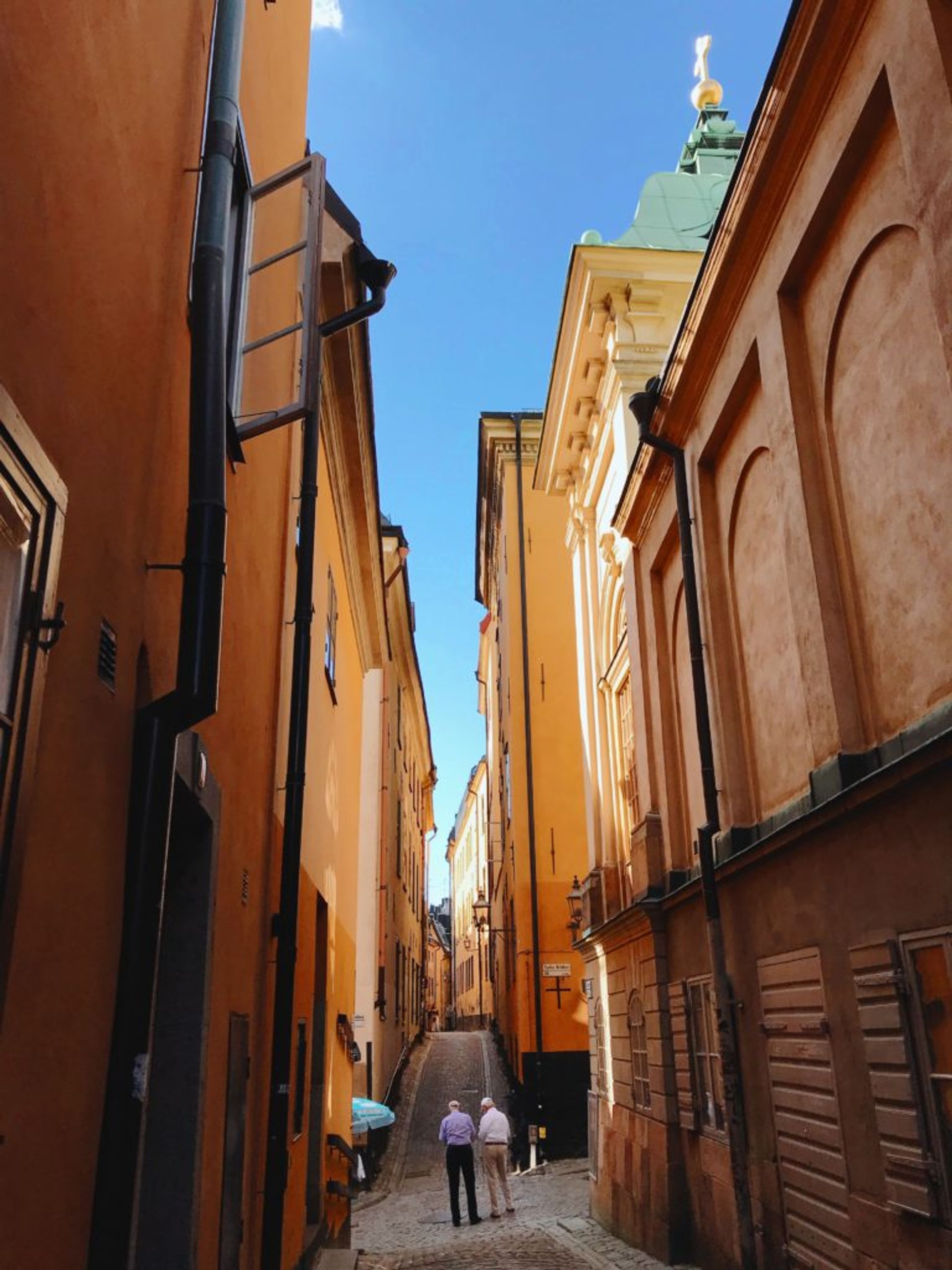 Two older men walking down a narrow, cobbled street in Stockholm's Old Town.