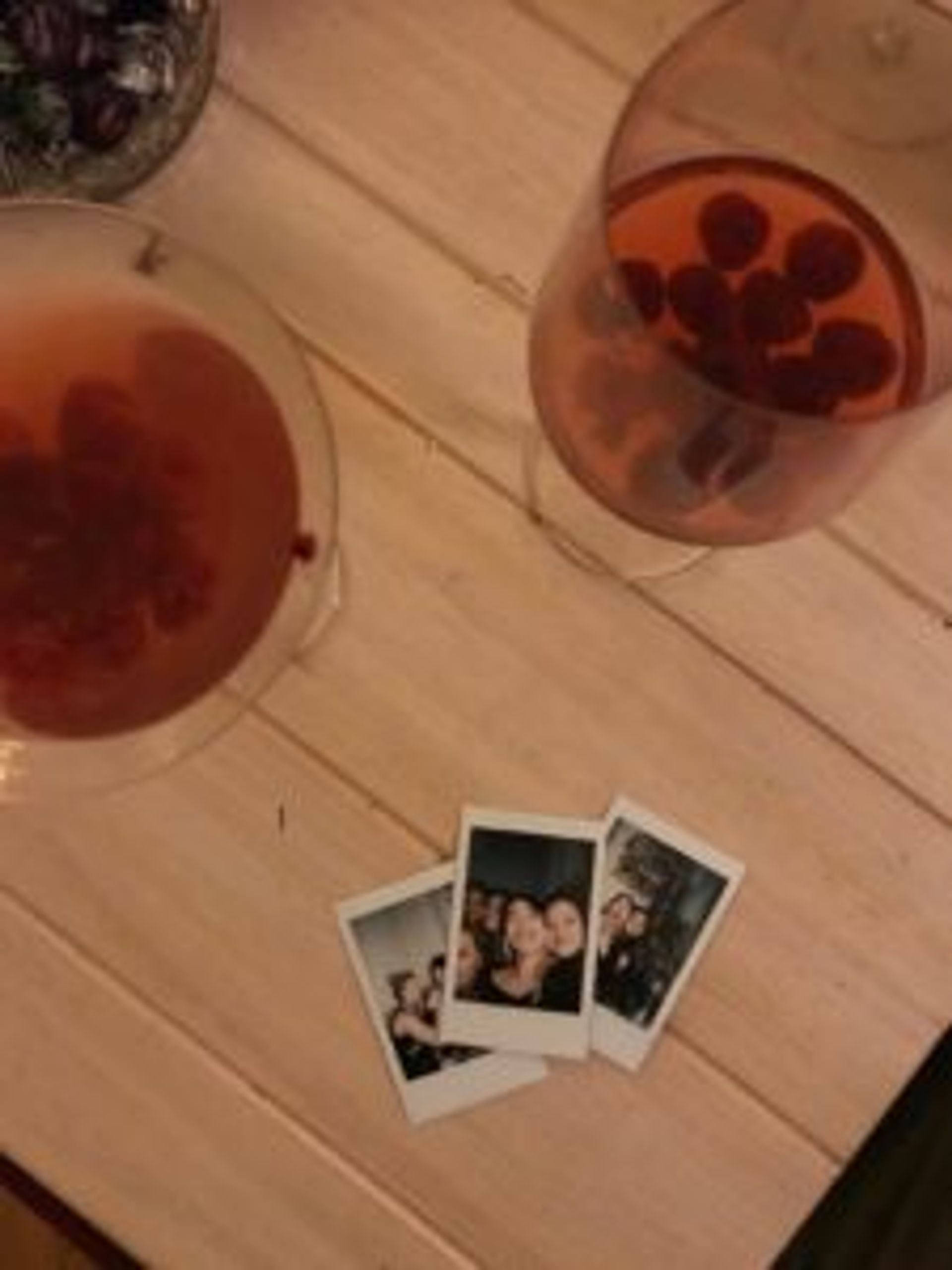 Two wine glasses and there Polaroid photos on a table.