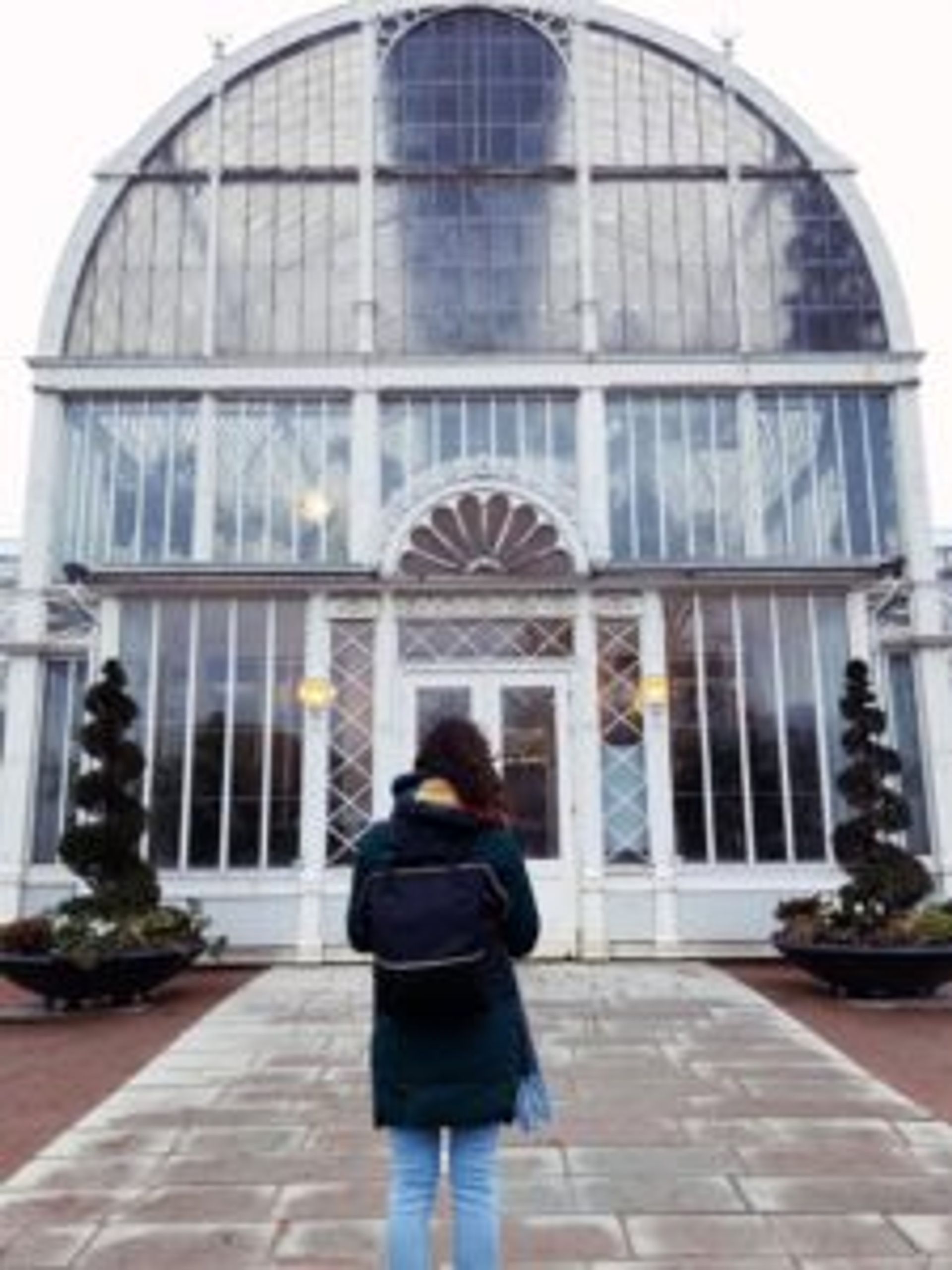 A person standing in front of the large, white greenhouse.