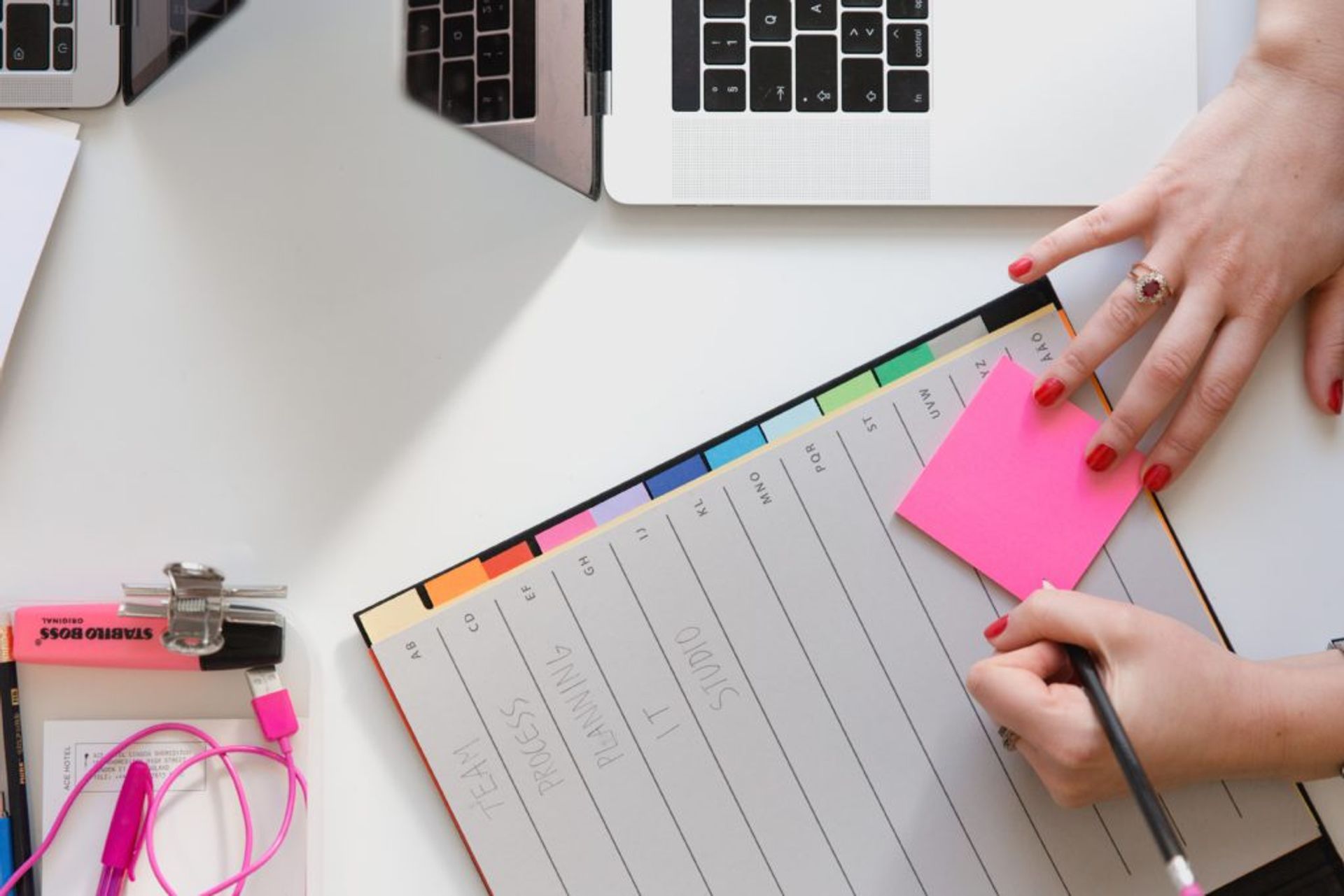 A woman writes on a pink sticky note.