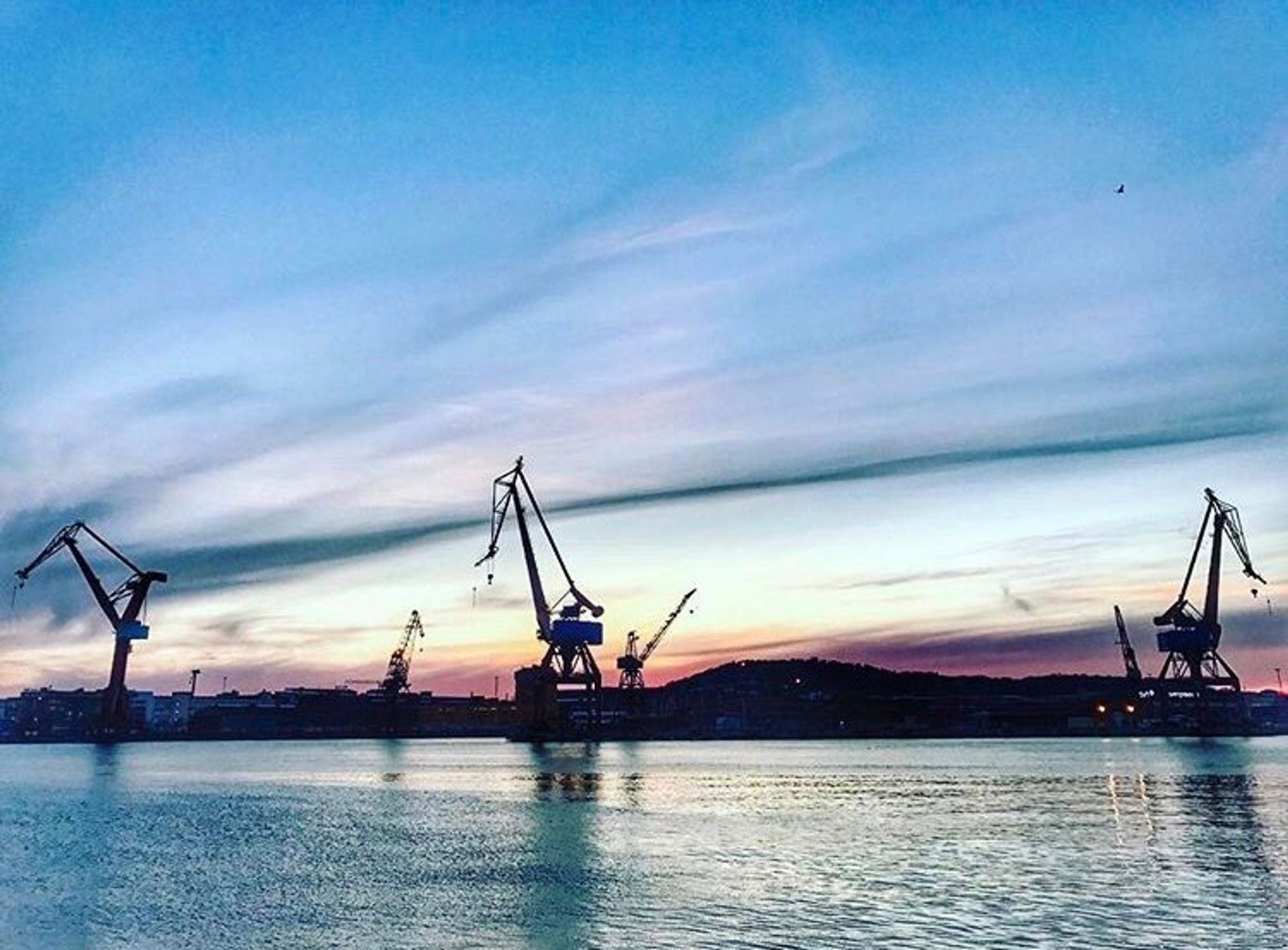 Construction cranes silhouetted against a sunset.