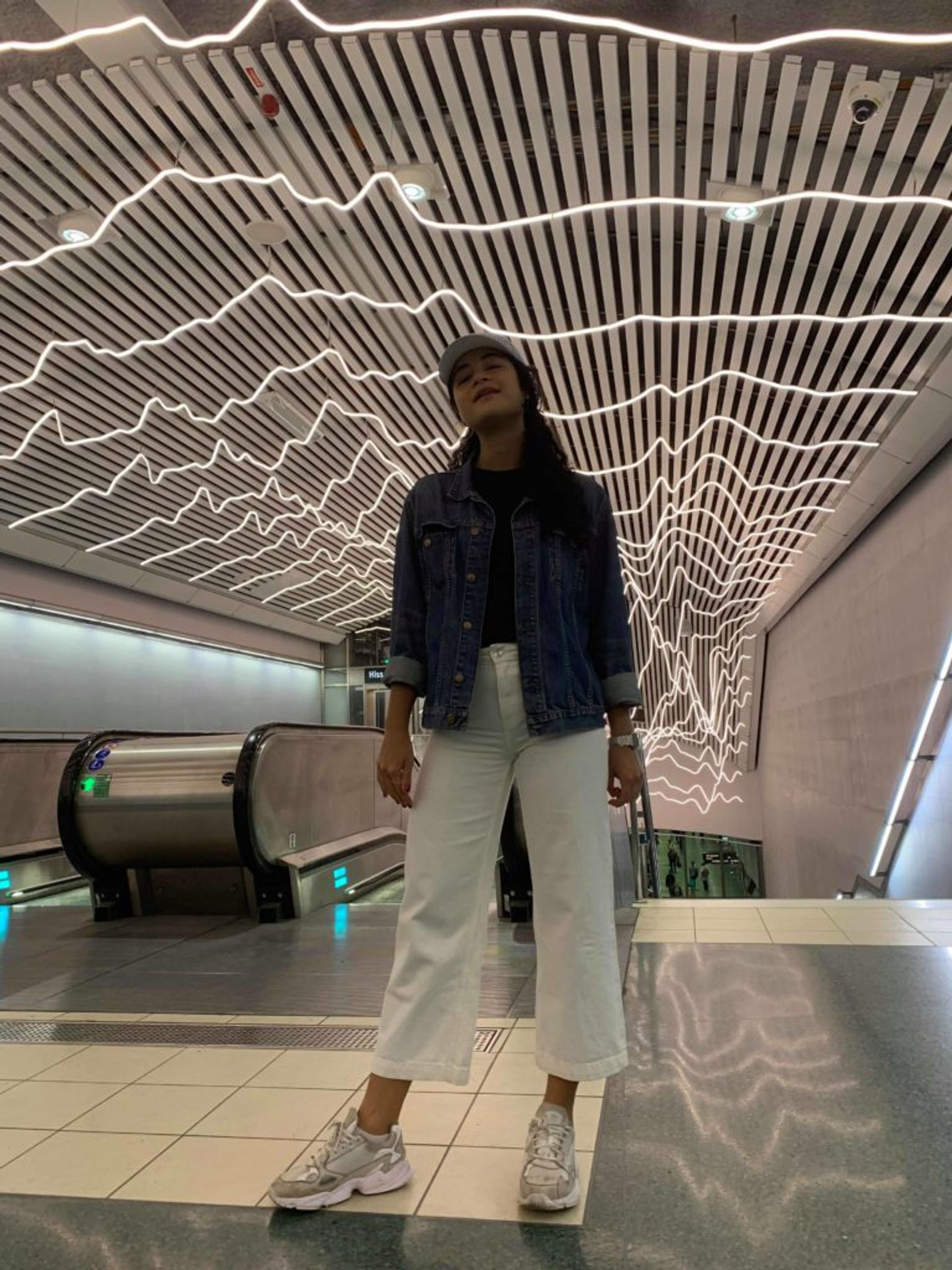 Marina stands in the Stockholm metro in cropped, white jeans, white sneakers and a denim jacket.