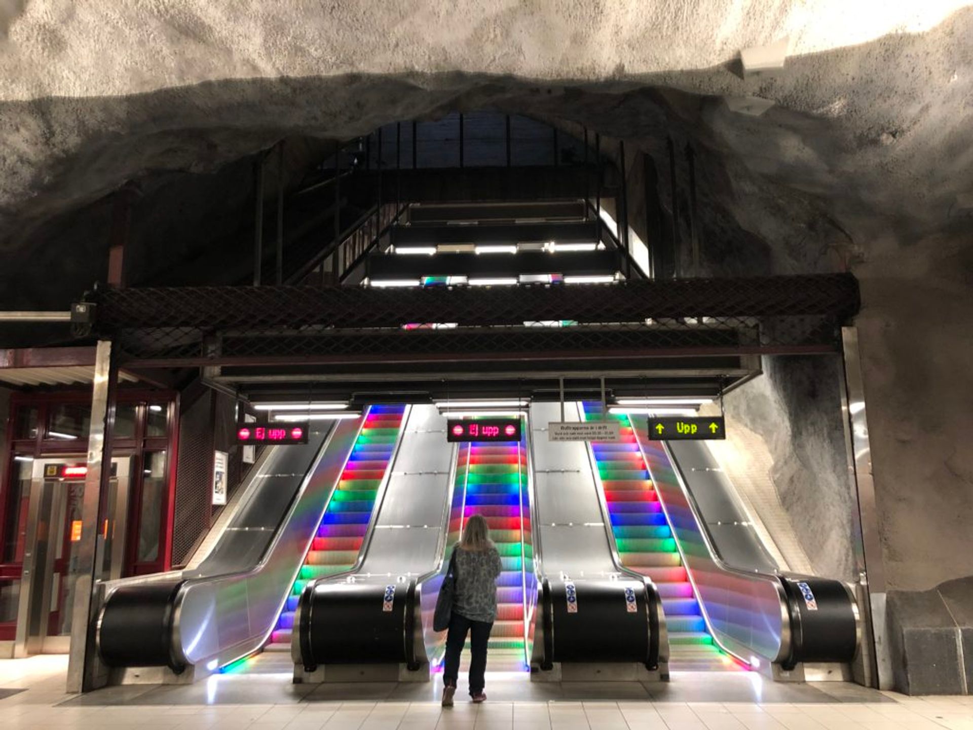 Three escalators in the Stockholm metro. The escalator steps are lit up in the colours of the rainbow.