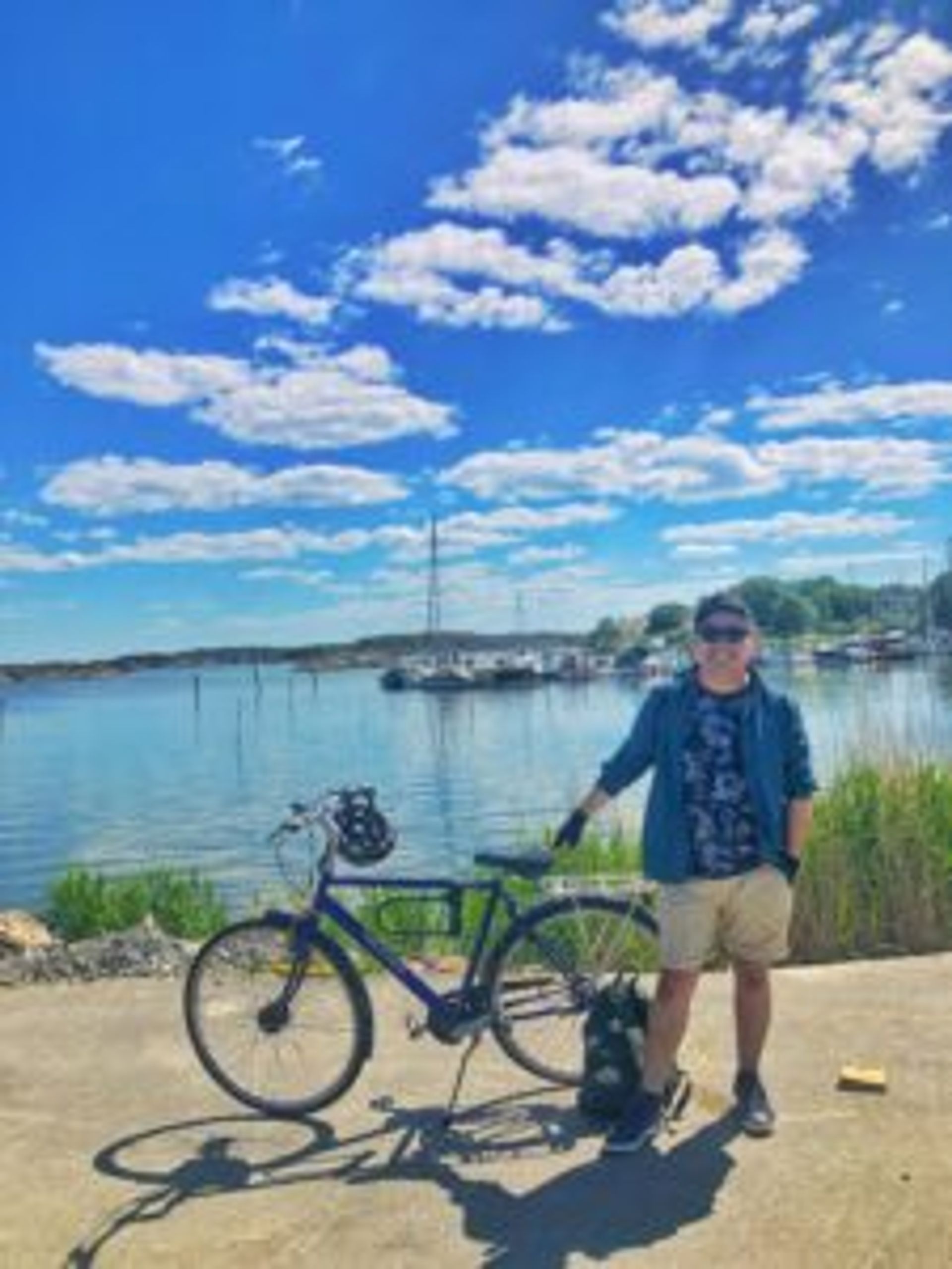 Camilo stands holding his bike in front of a lake.