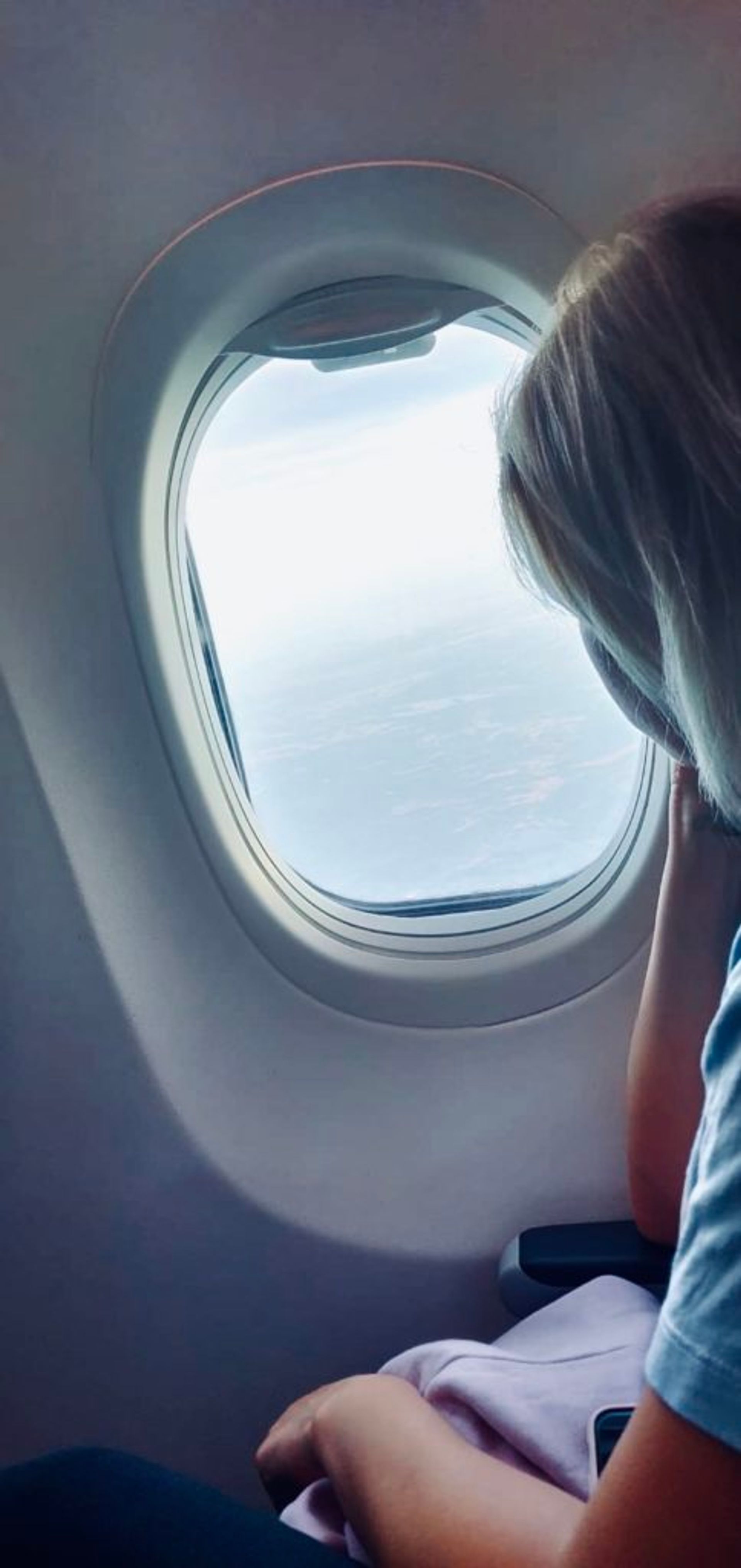 Sara sitting on an airplane, looking out of the airplane's window at the land below.