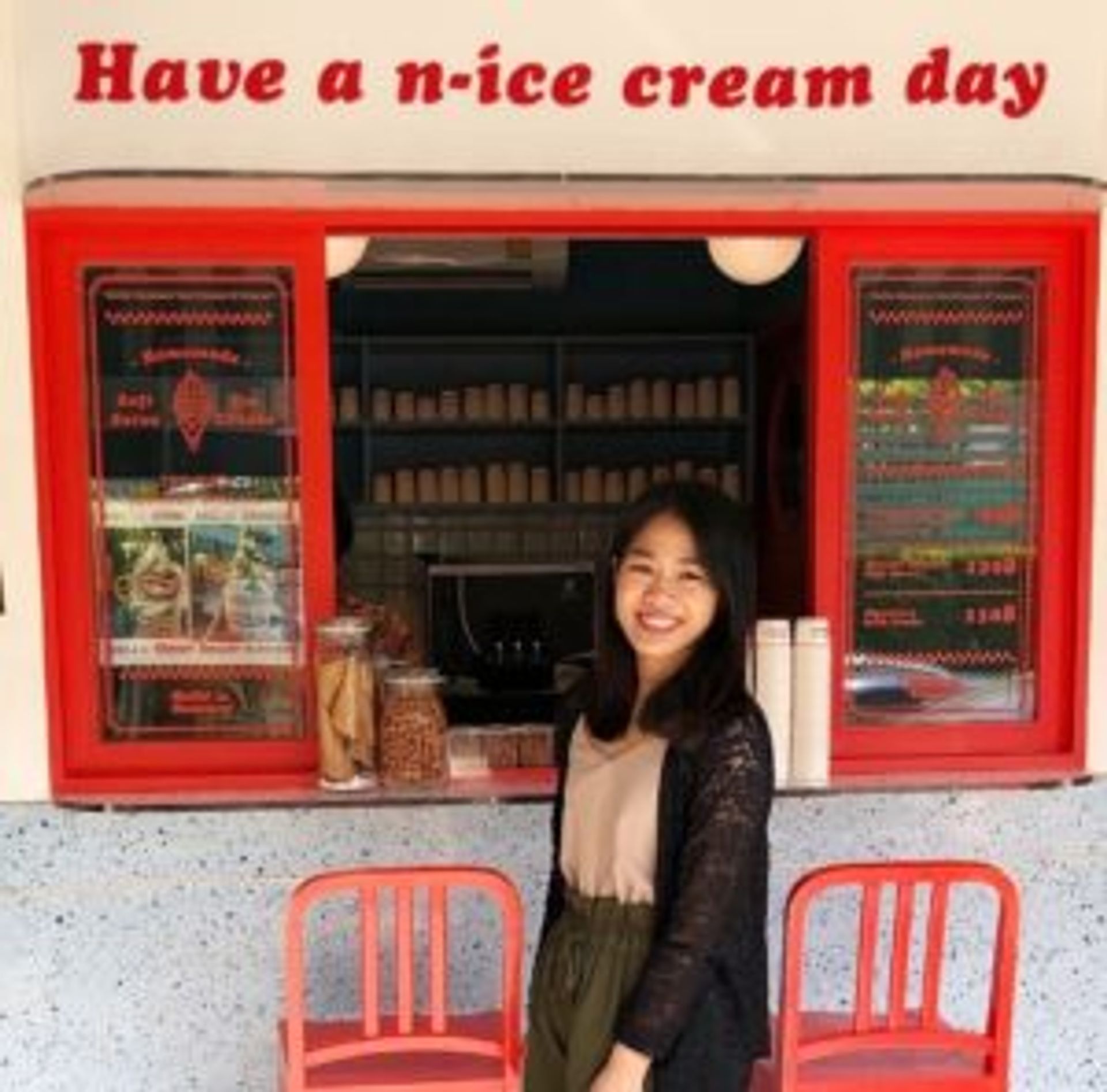 Arisa standing in front of a small ice-cream shop. The shop has a sign that reads 'Have a n-ice cream day'.