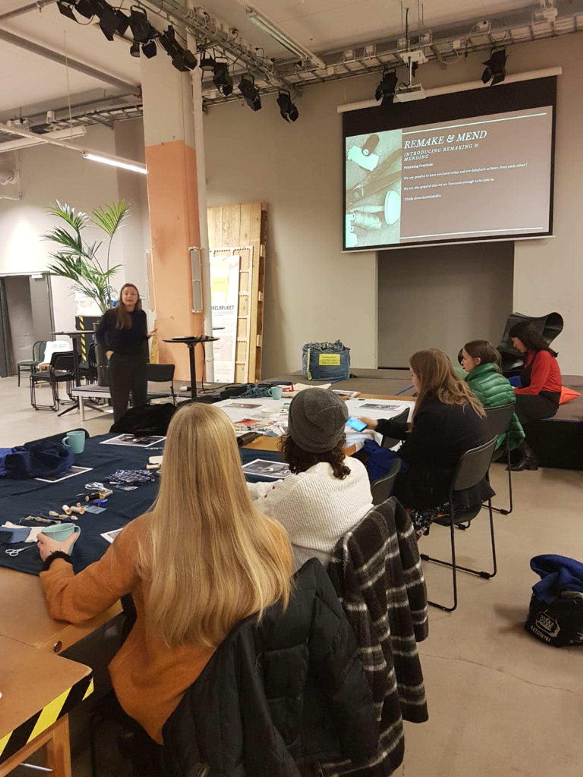 A woman gives a presentation about the remake and mend workshop to a group of students.