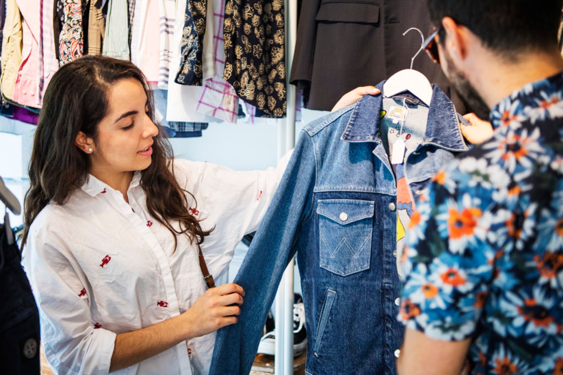 Two people in a second hand shop looking at a denim jacket.