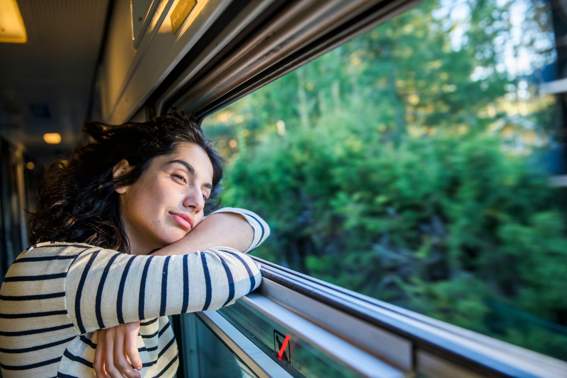 A dark-haired woman wearing a stripy top staring out of a train window.