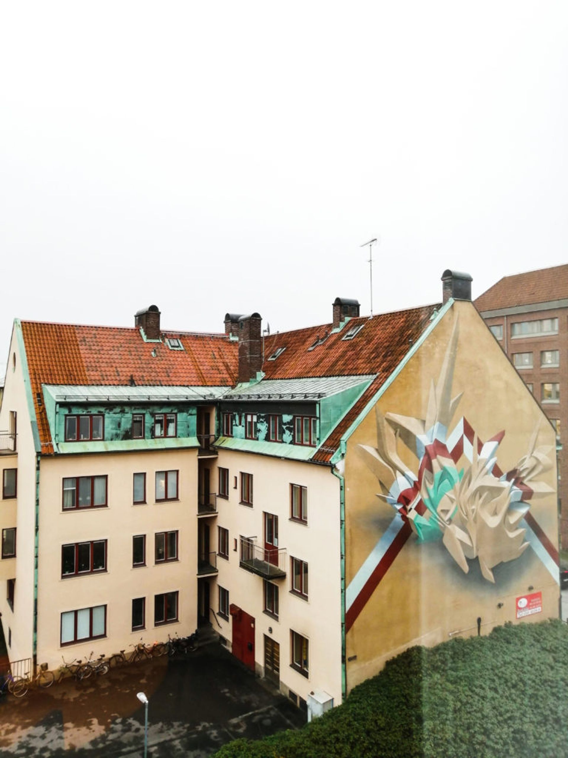 Abstract mural with contrasting stripes of rust, white and minton the side of a residential building.