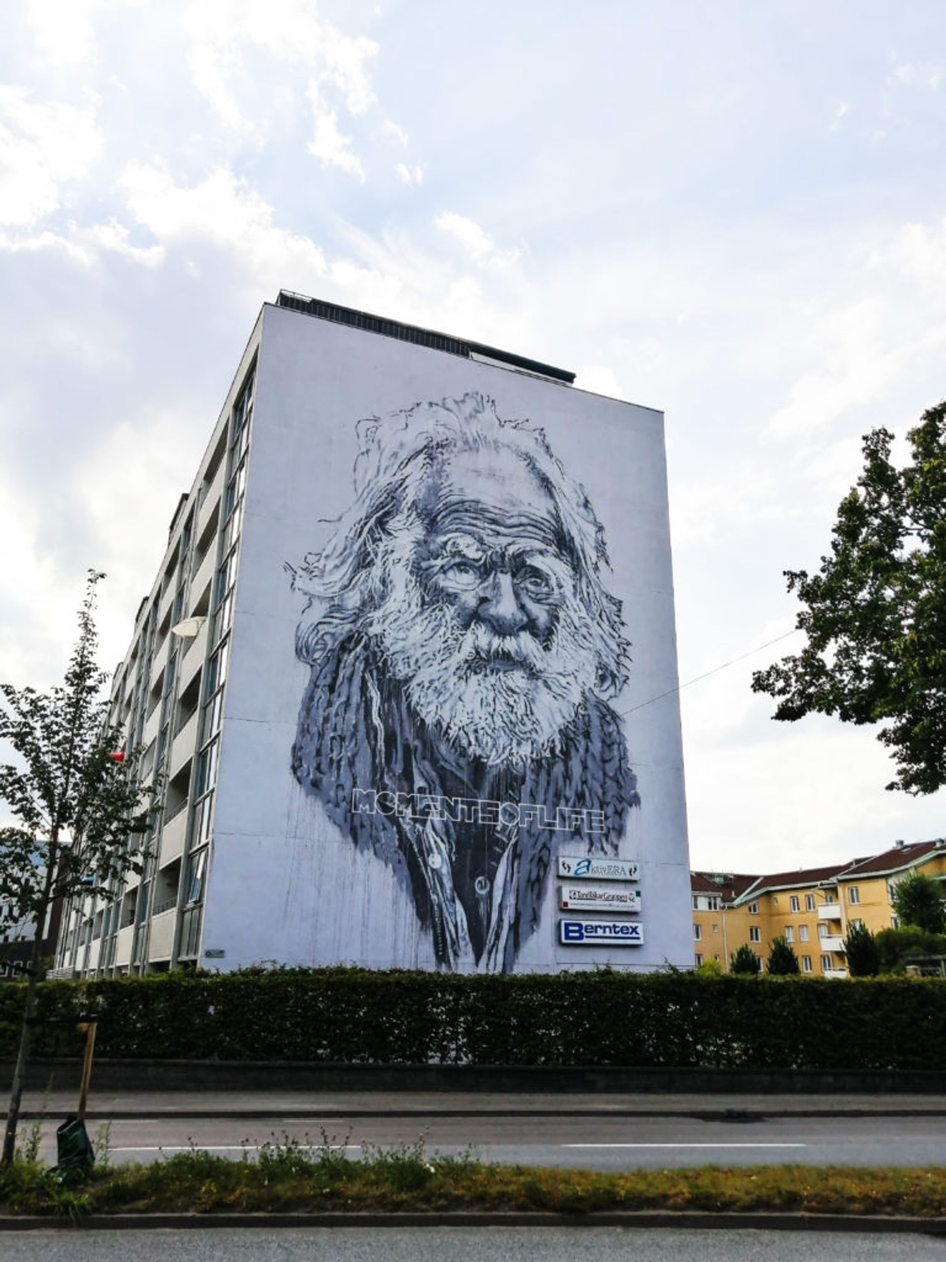 Realistic black and white mural of elderly man with text 'Moments of Life' on the side of a residential building in Borås. 