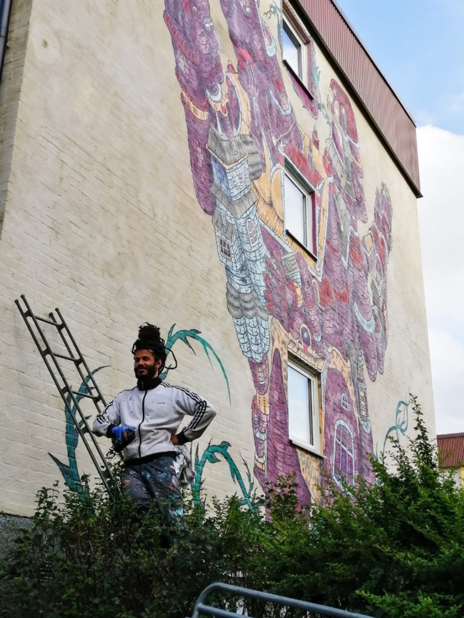 An artist stands on a ladder in front of the mural he is painting.