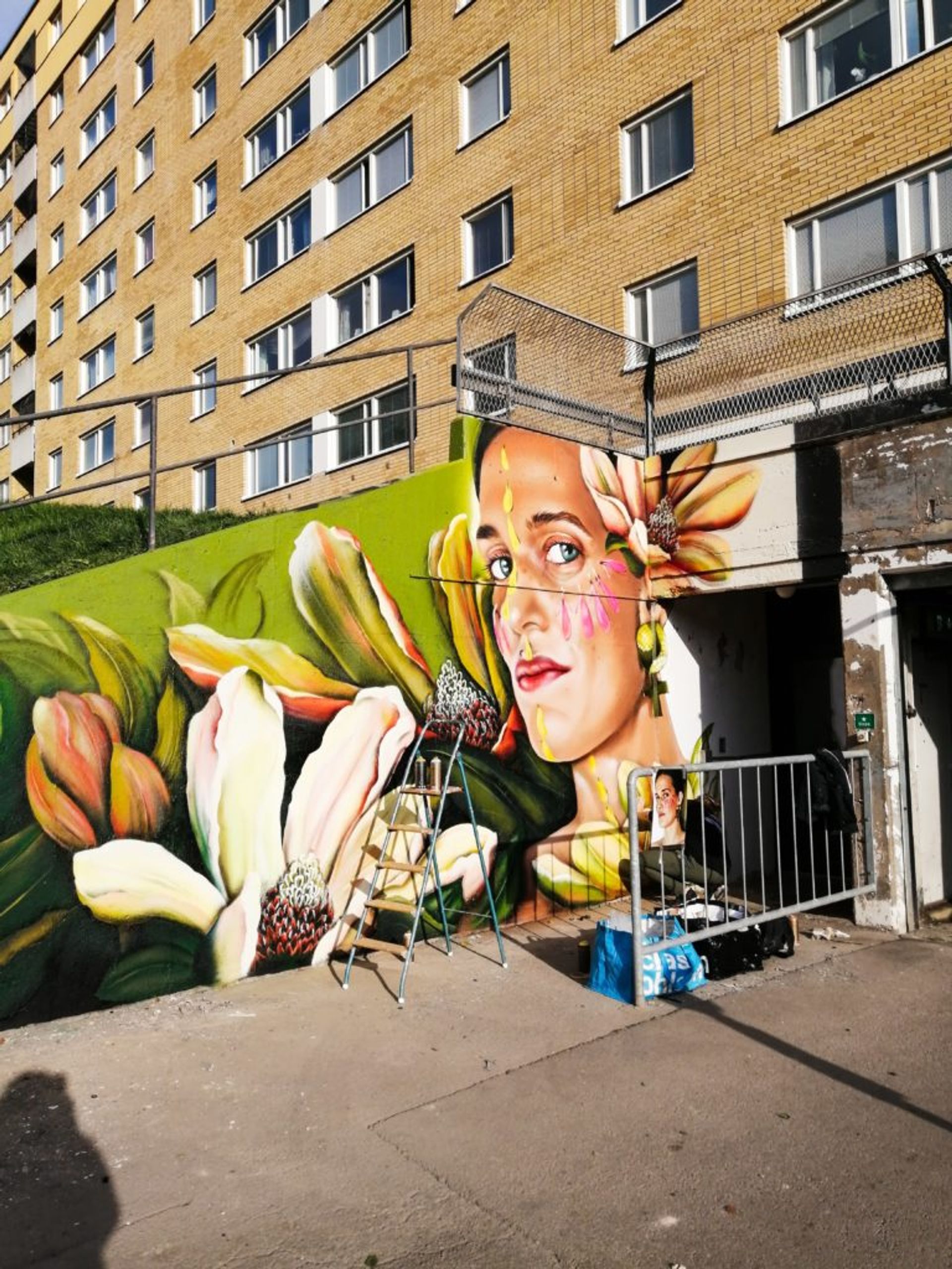 Photorealistic portrait of woman surrounded by flowers on a concrete wall.