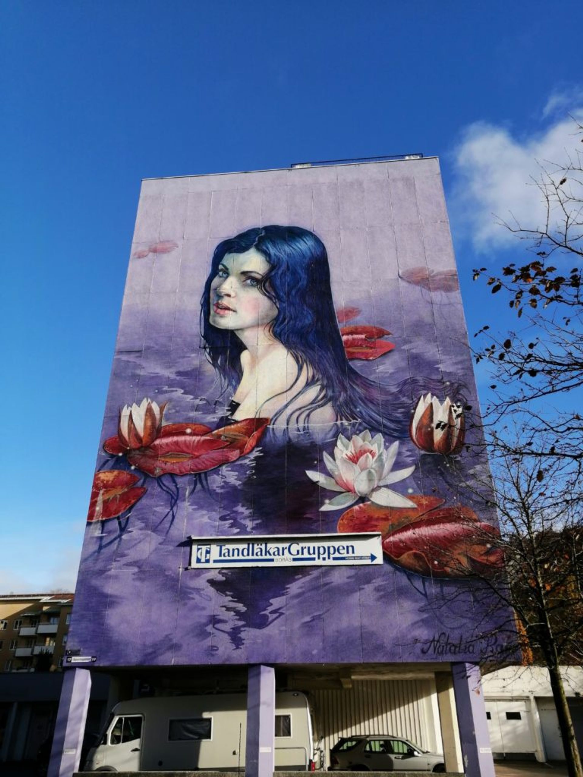 Mural of a woman swimming in purple and blue water on the side of a residential building in Borås.