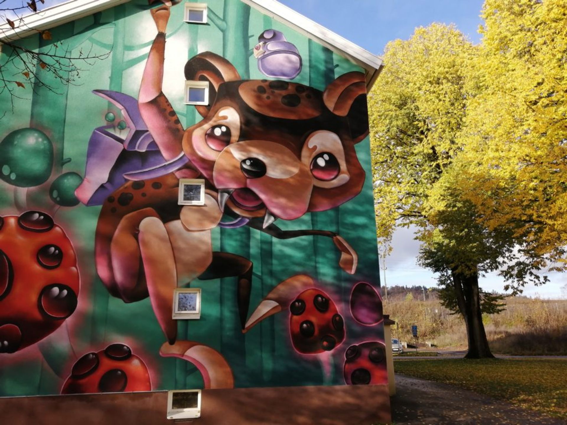 Colourful mural of cute and playful animalistic creature on the side of a residential building.