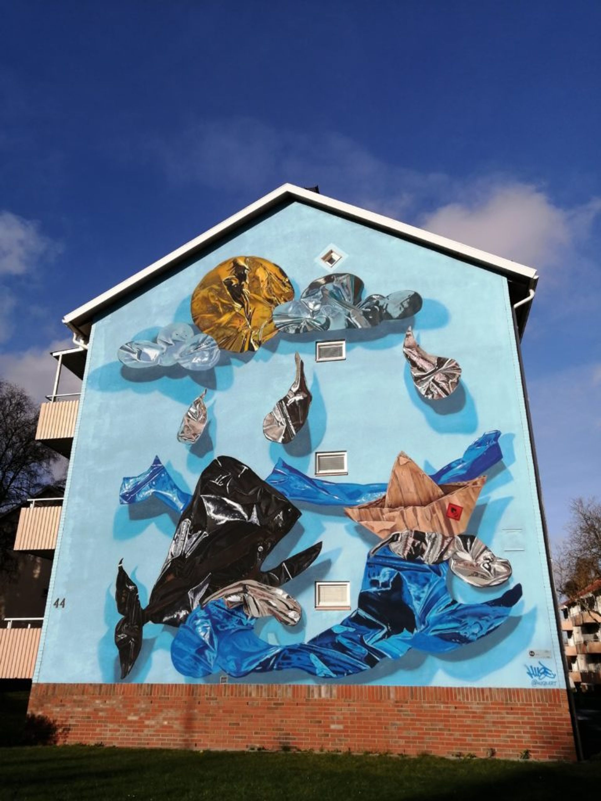 Mural of hyper-realistic balloon whale swimming in litter on the side of a residential building in Borås.