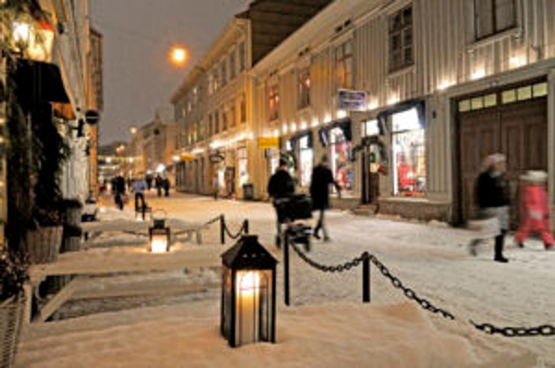 People walking down a snowy street lit up by Christmas lights.