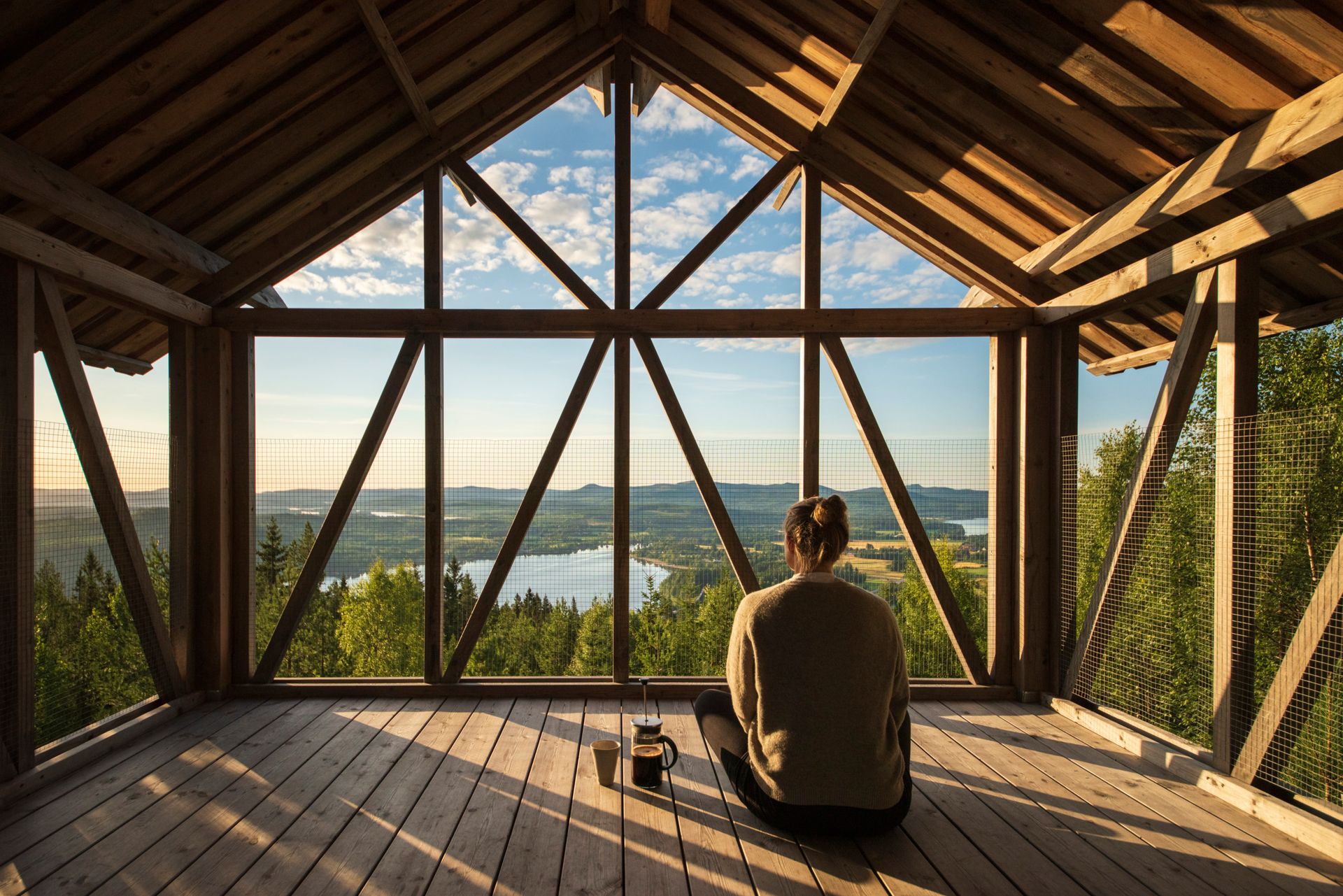 A person sitting inside a wooden construction amongst the treetops a Swedish forrest looking at the view.
