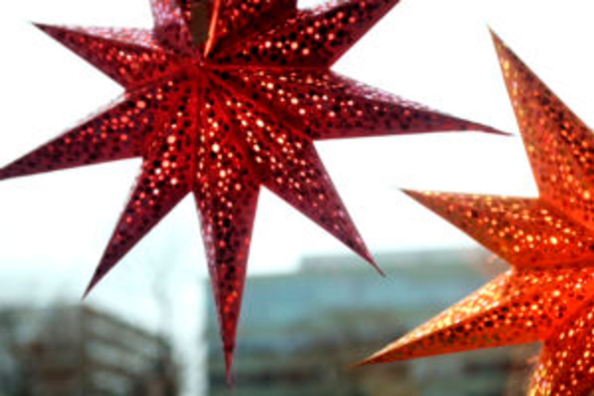 Two red, sparkly paper star decorations hanging in a widow.