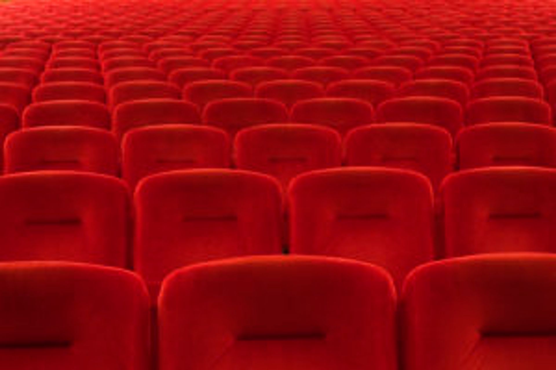 Rows of red velour cinema theatre seats. 