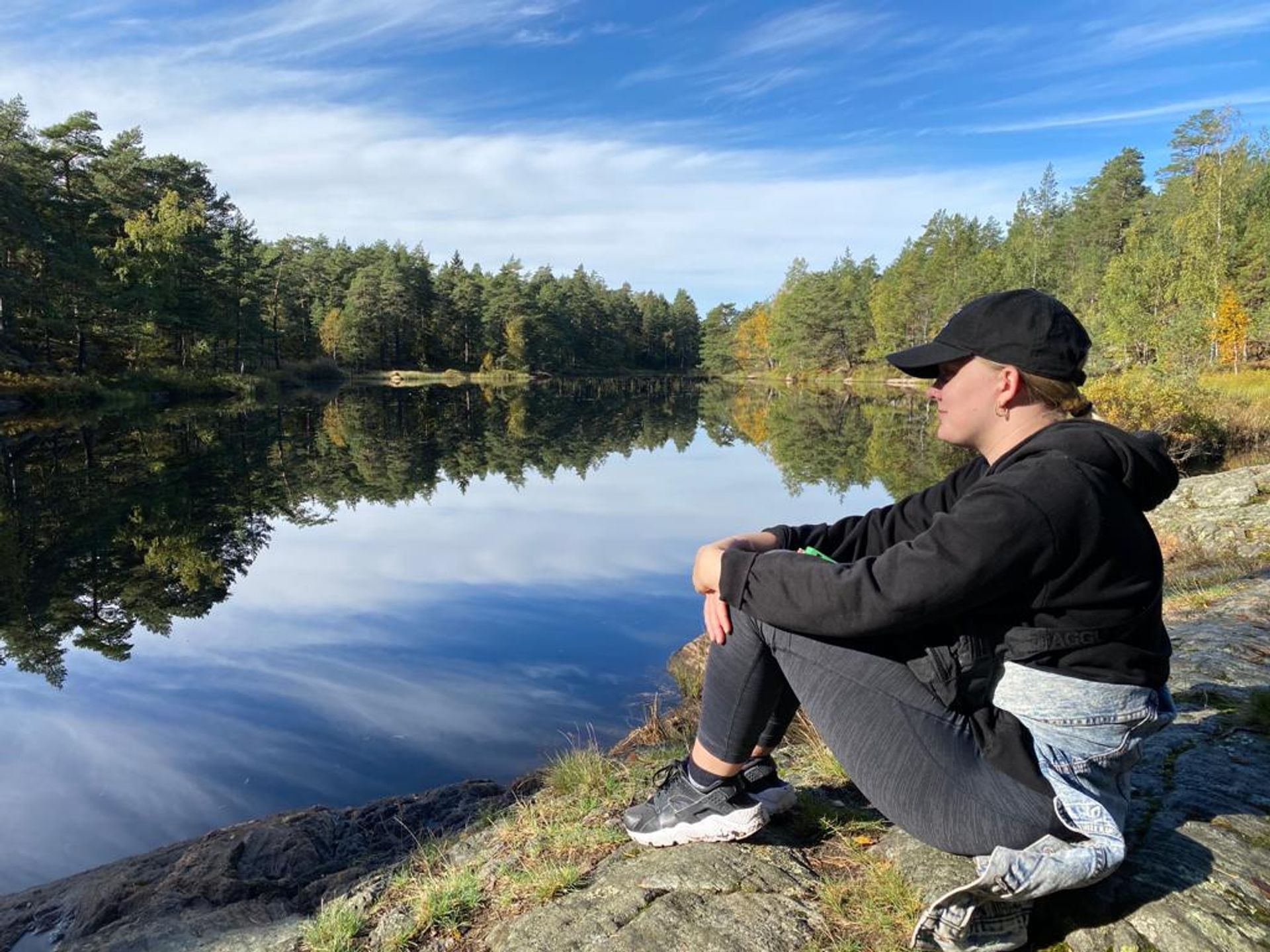 Brooke sitting alongside a lake surrounded by trees