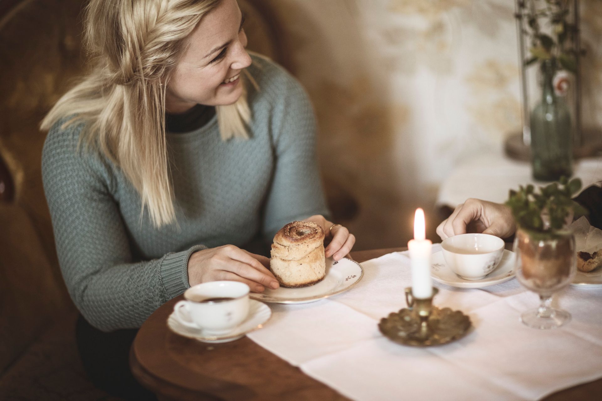 A woman sitting in a cafe drinking coffee and eating a cinnamon bun.