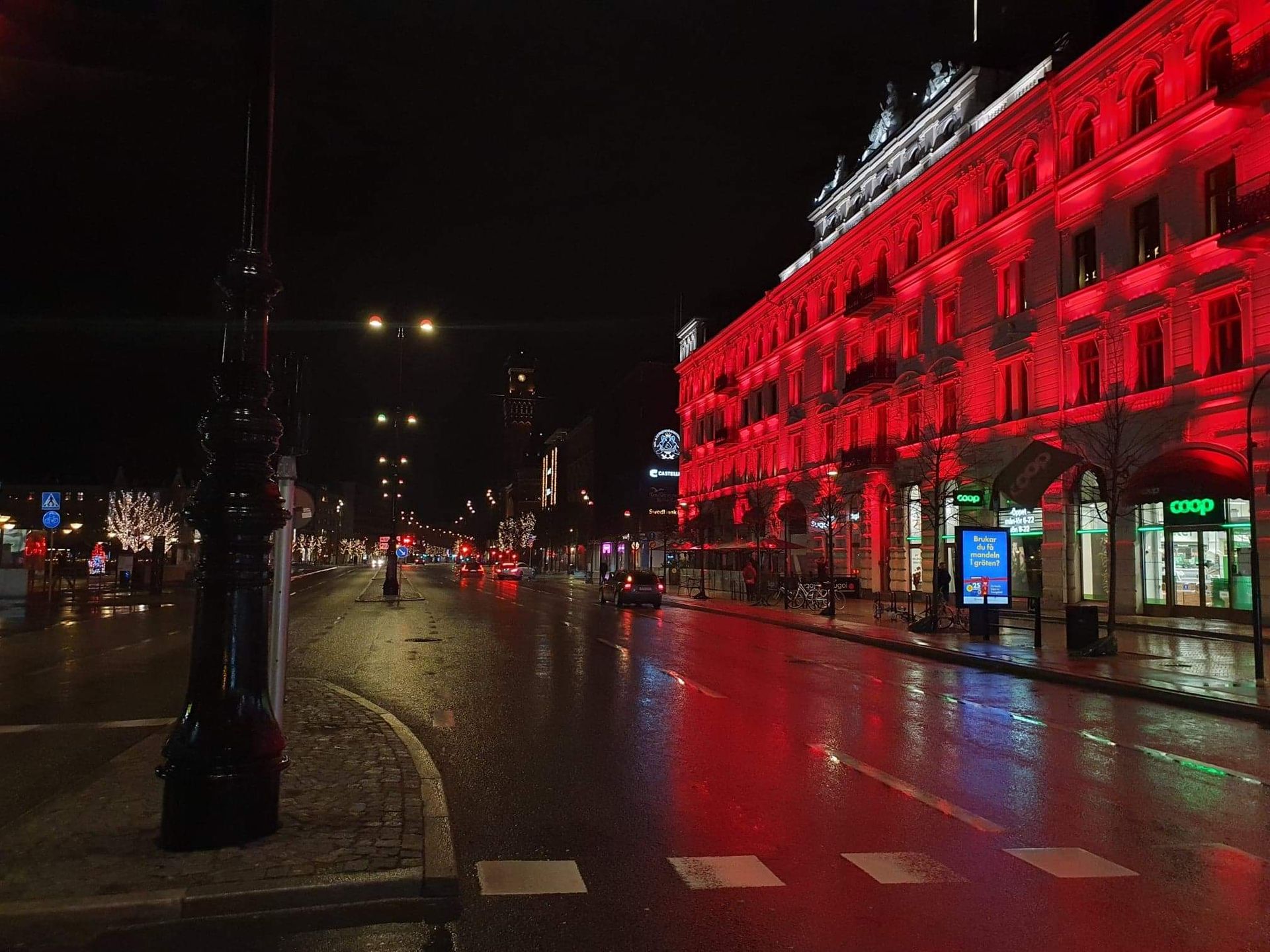 Dark evening, a wet glistening street in front of a building with bright red lights