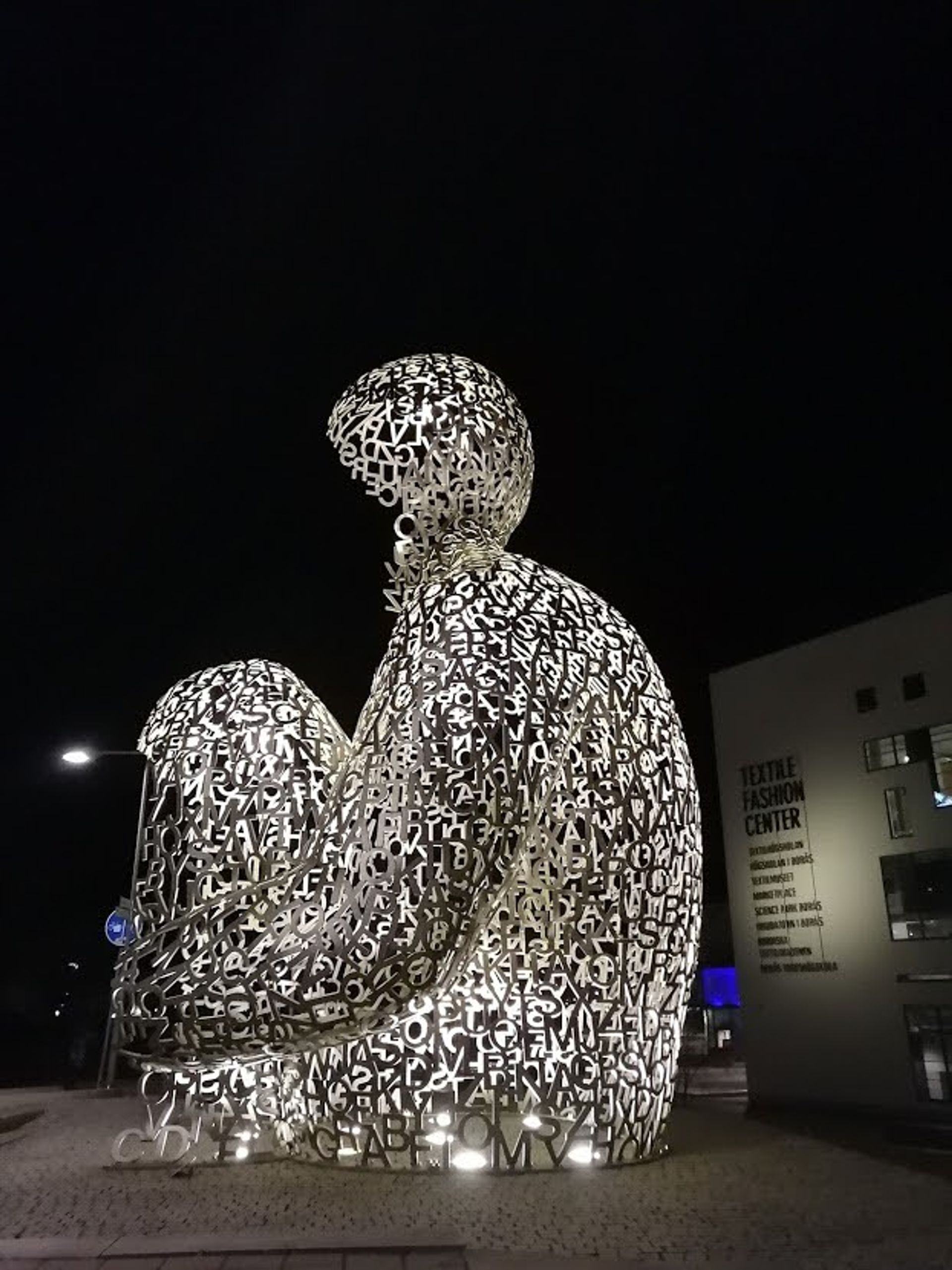 Hollow sculpture of a body sitting cross-legged, made out of cut-out shapes and letters