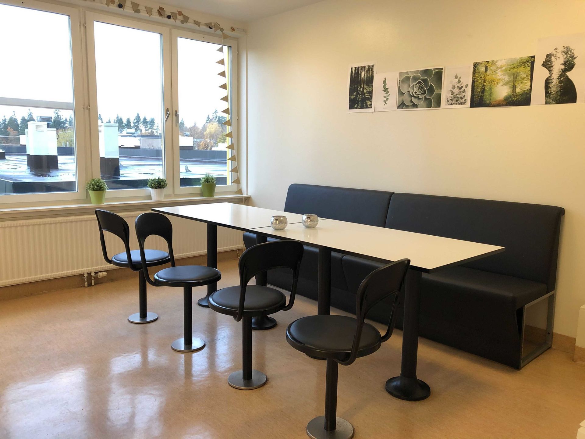 A shared common space with four black chairs, a table and a couch in front of a window