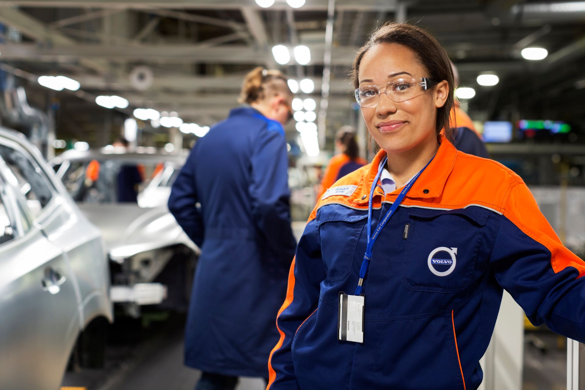 A proud woman engineer standing in front of a car wearing a Volvo uniform