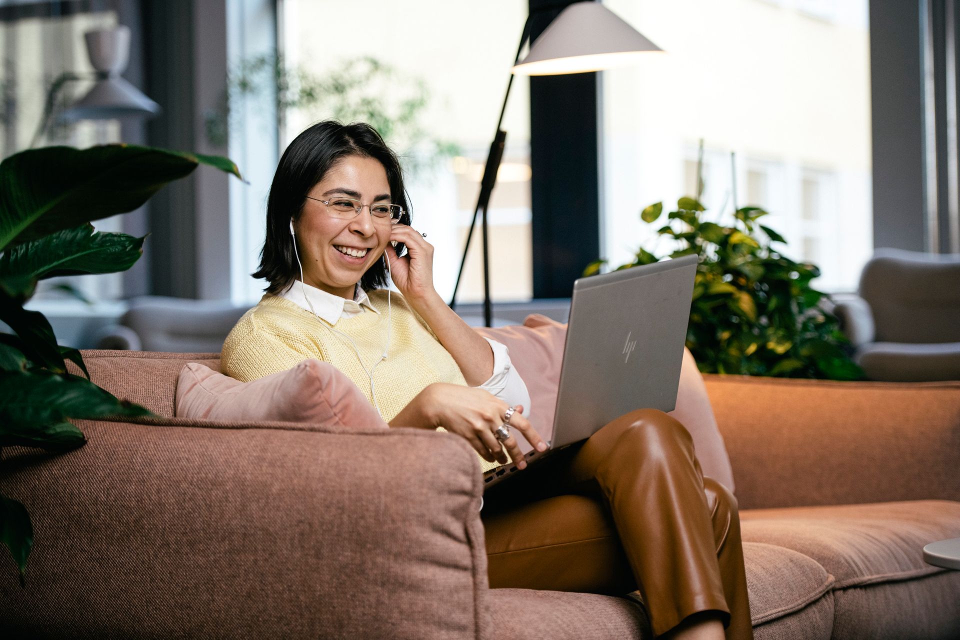 A woman sits in an arm chair with a laptop and earpieces.