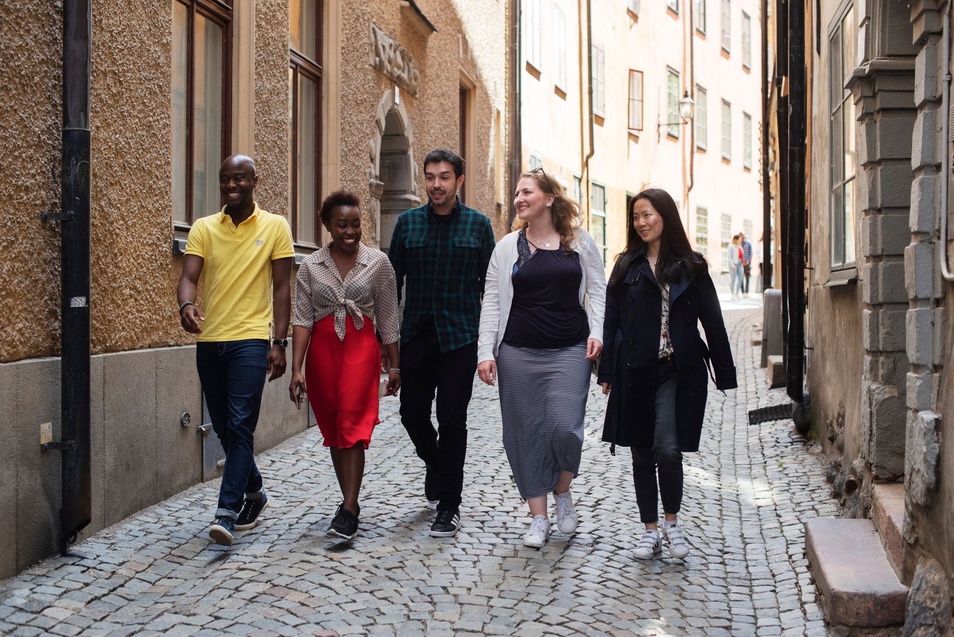 A group of friends are walking down a narrow cobbled street, smiling.