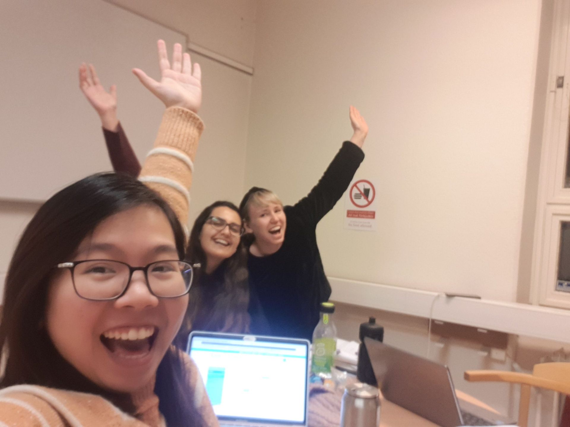 Three young ladies throw hands in the air to celebrate the end of a successful group project
