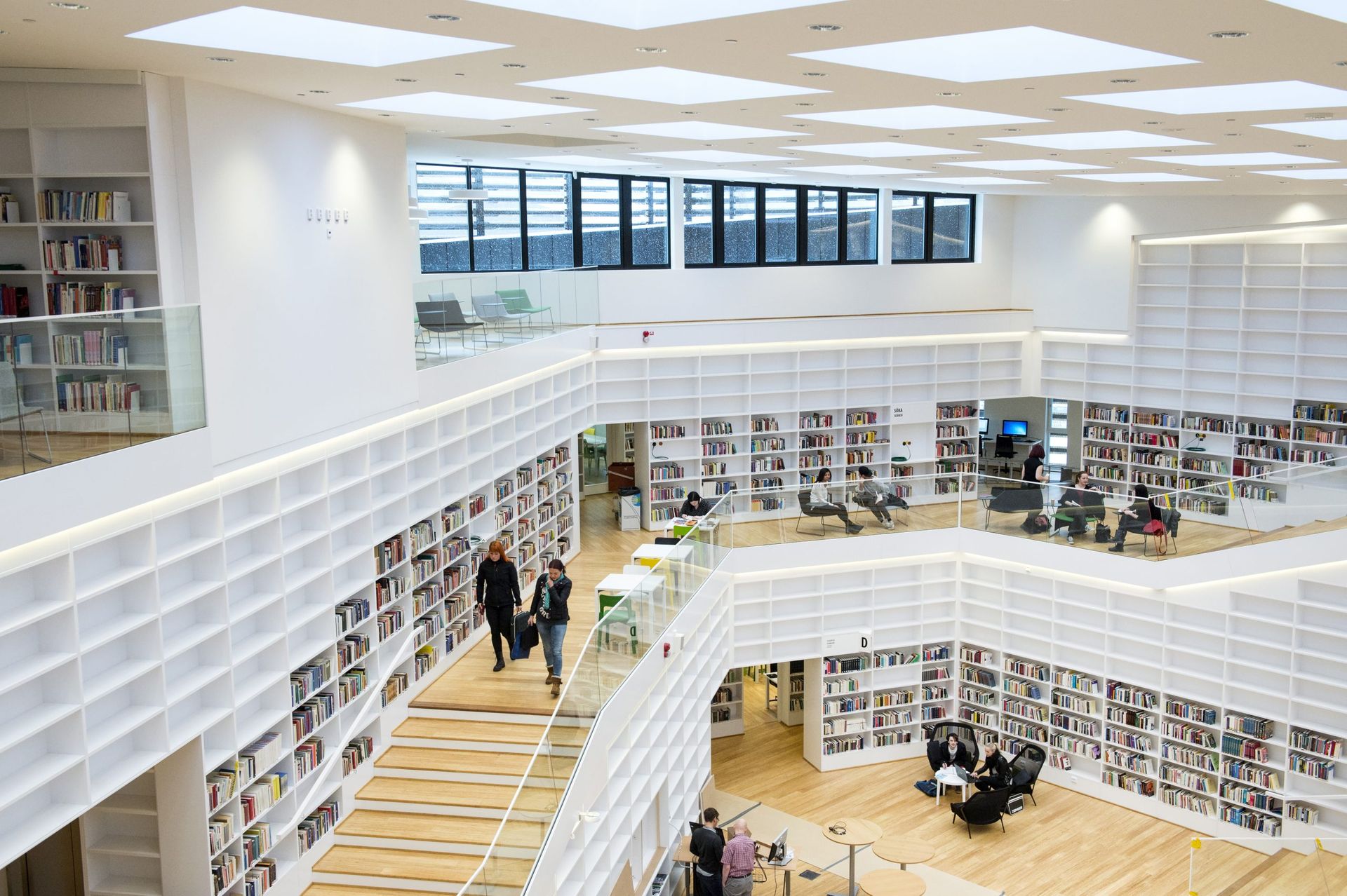 Inside of a bright library with white bookshelves and students studying and walking