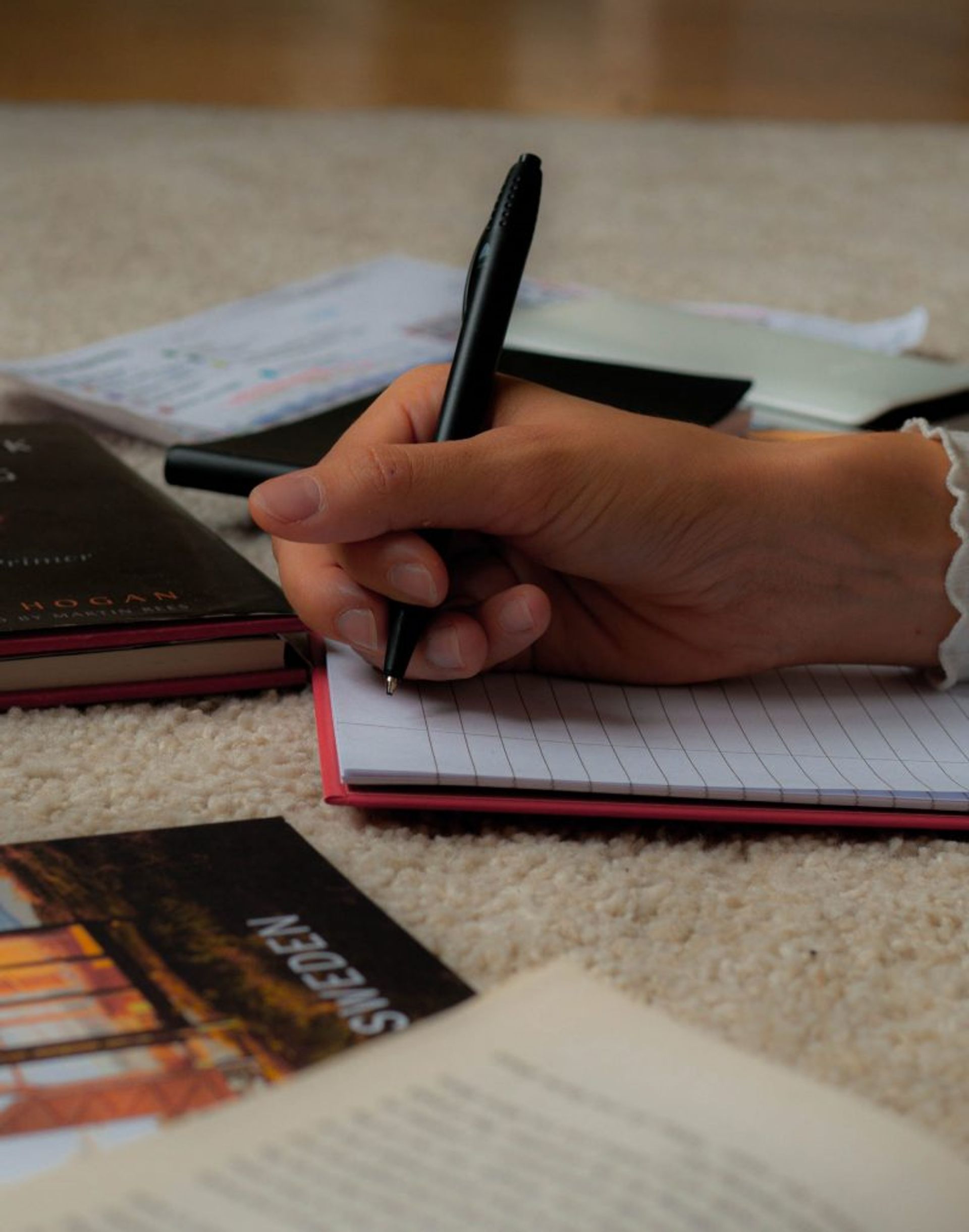 A hand writing on a notebook with a black pen.