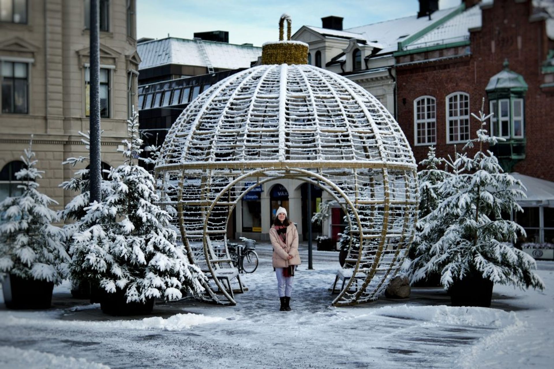A girl posing in front of a seating spot that looks like a large Christmas bulb. 